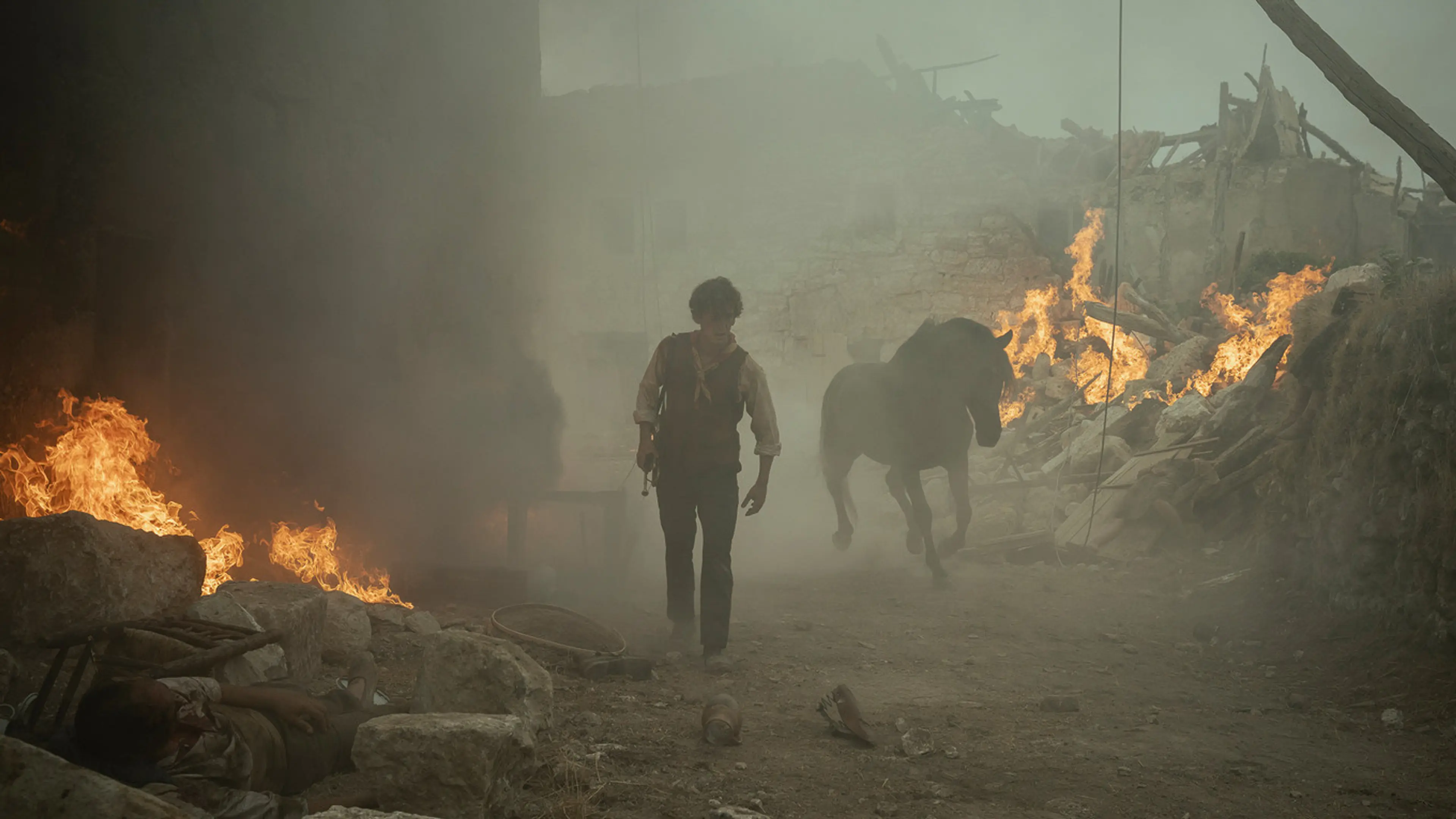 Sebastián walks beside a horse through smoke and burning rubble after a bombing.