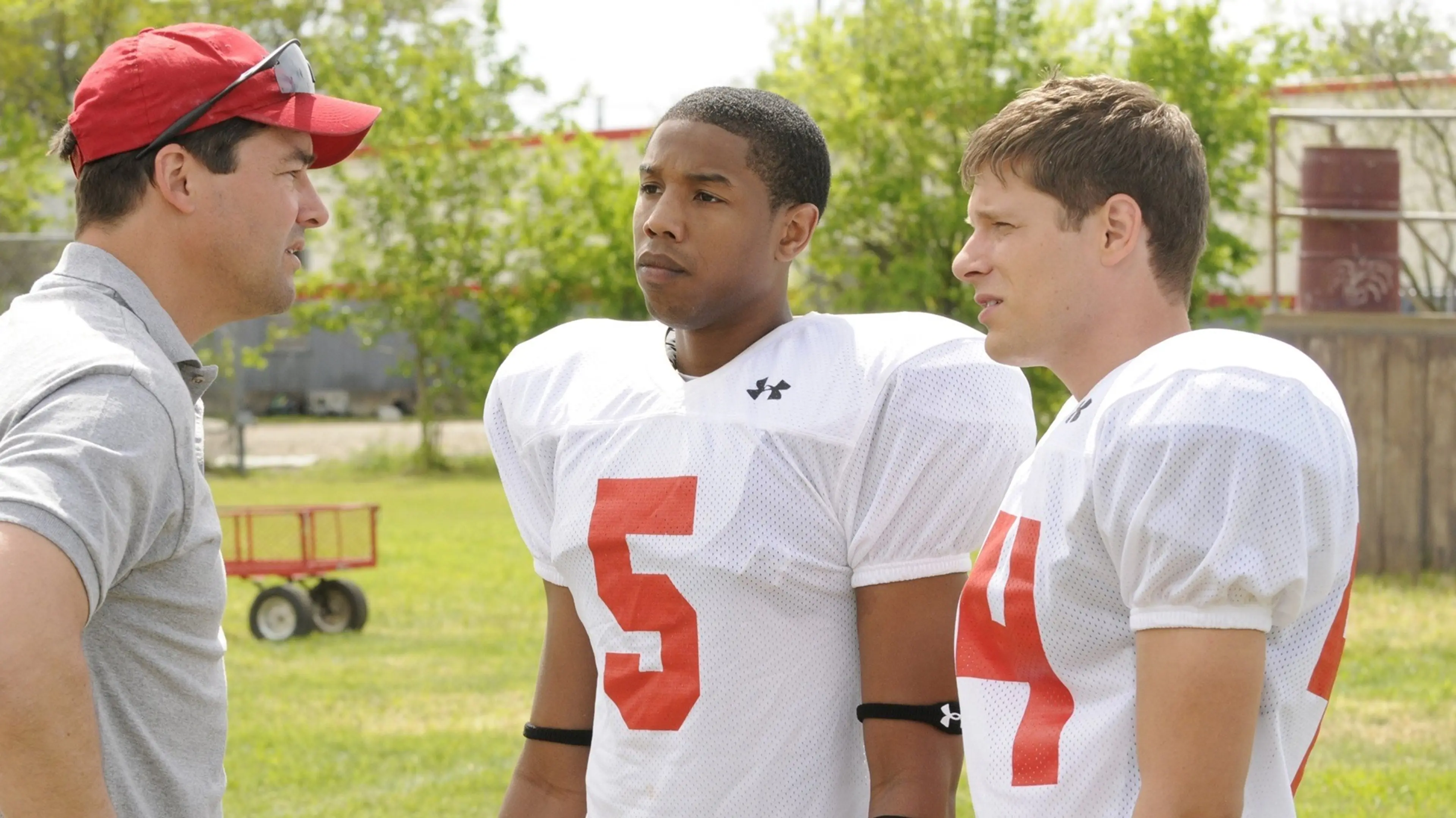 Kyle Chandler speaks with Michael B. Jordan and another football player on a field in Friday Night Lights.