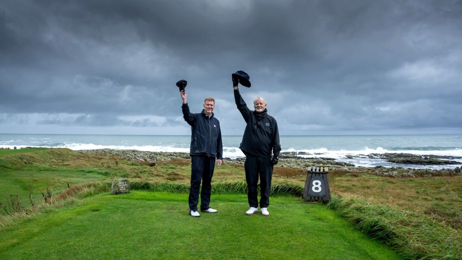 Tom Coyne and Bill Murray raise their caps on an Irish golf course.