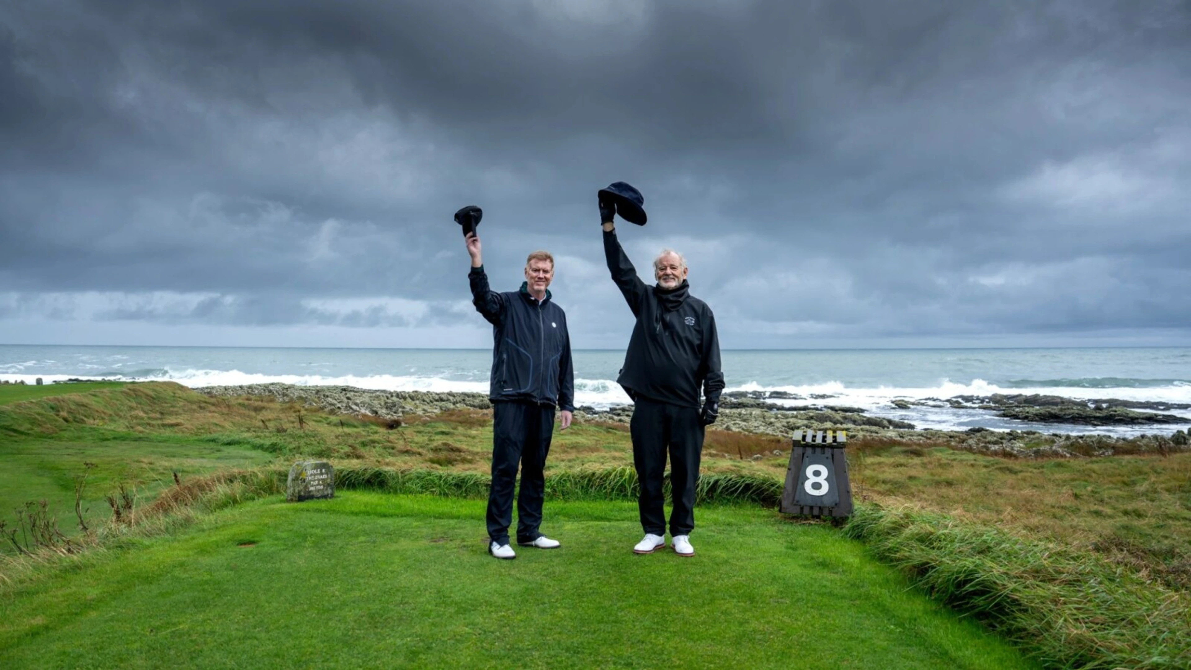 Tom Coyne and Bill Murray raise their caps on an Irish golf course.