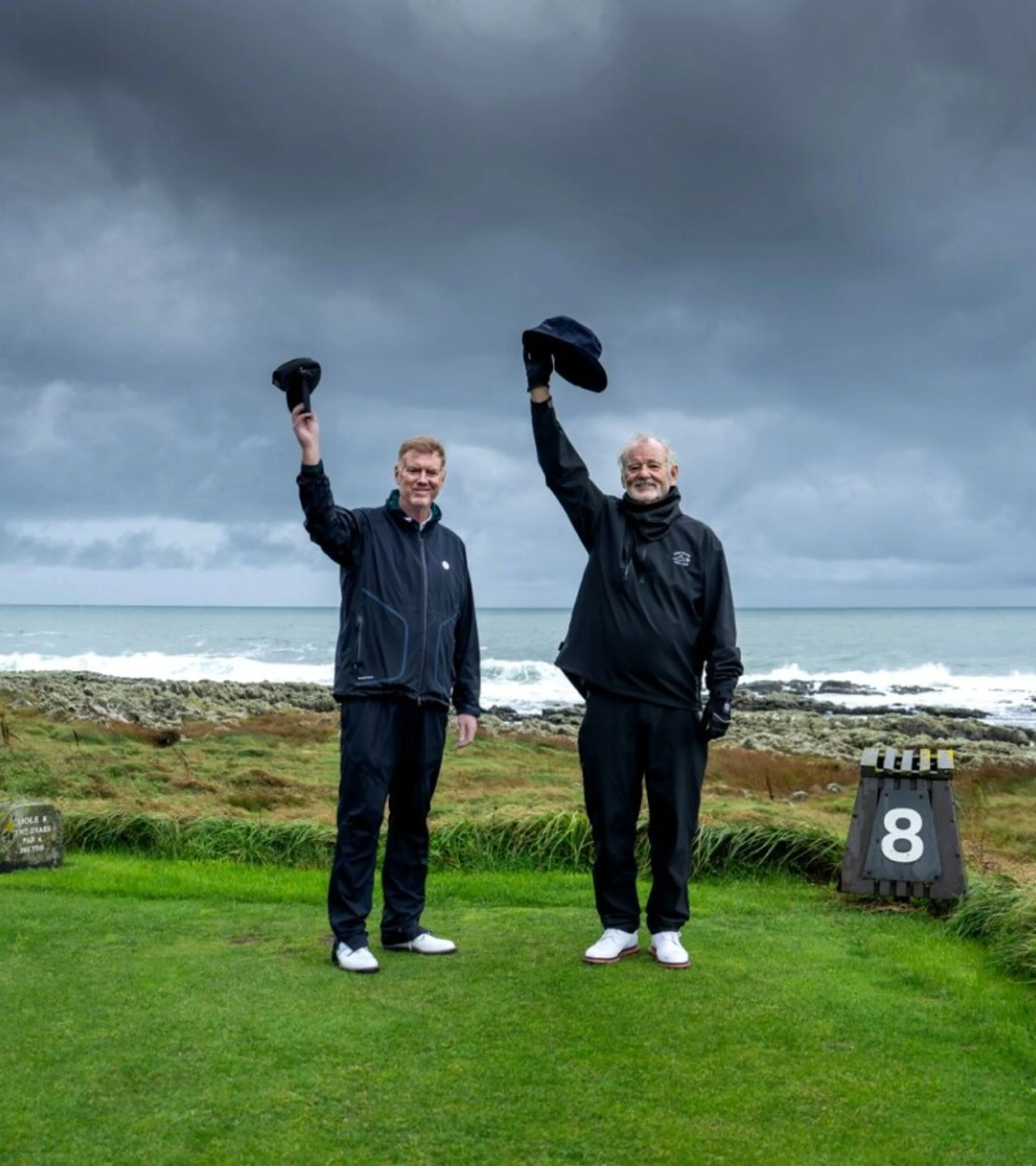 Tom Coyne and Bill Murray raise their caps on an Irish golf course.