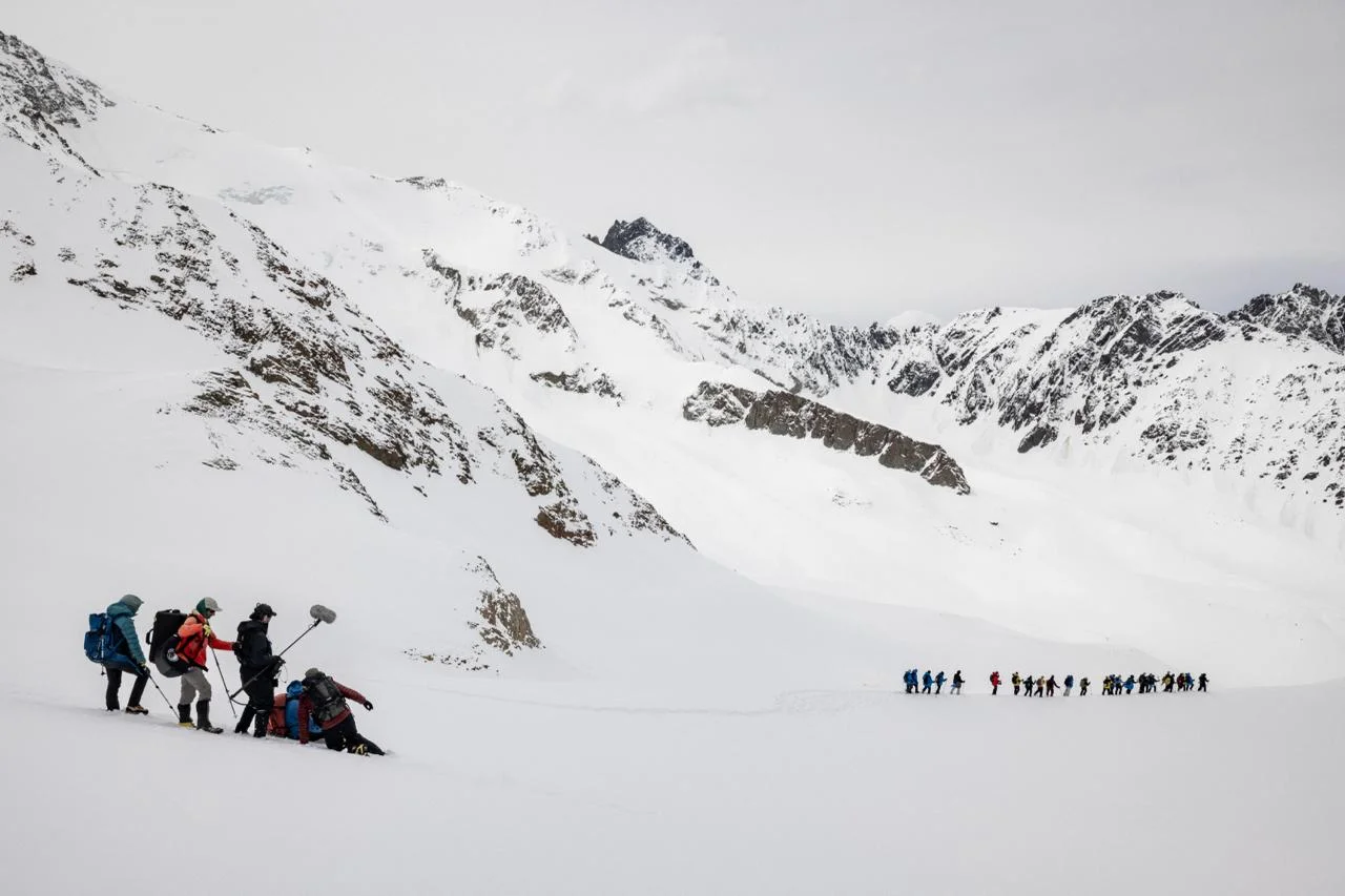 People and a film crew cross a broad snow-covered Andes landscape during production of Beyond Society.