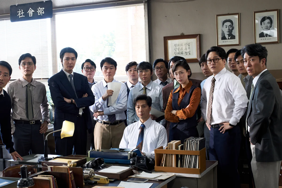 Reporters gather around a desk in the newsroom in The Assassin(s).
