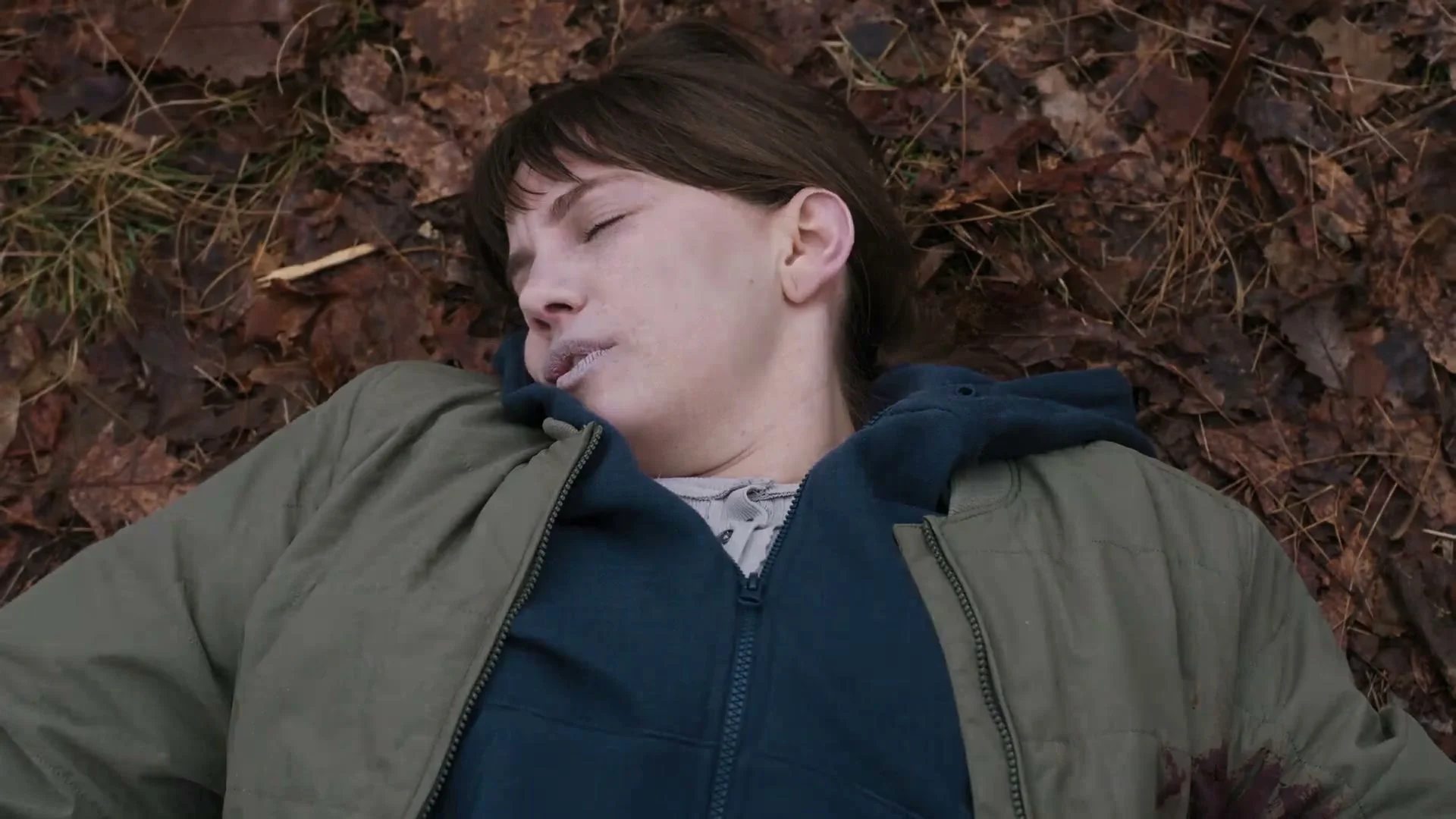 A young man lies on fallen leaves in a dark scene from Line of Fire.