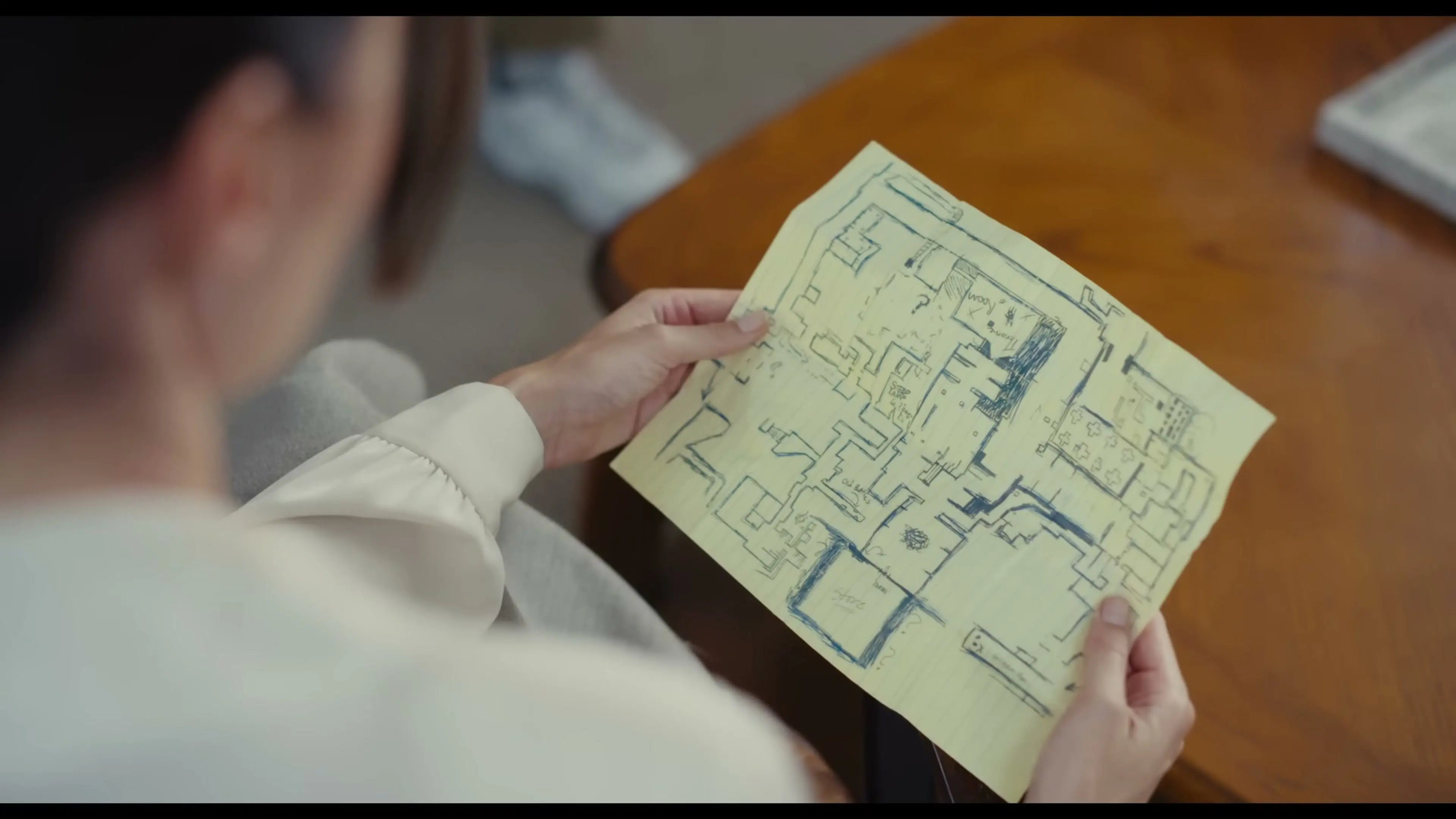A woman holds a hand-drawn floor plan covered in rooms and question marks.