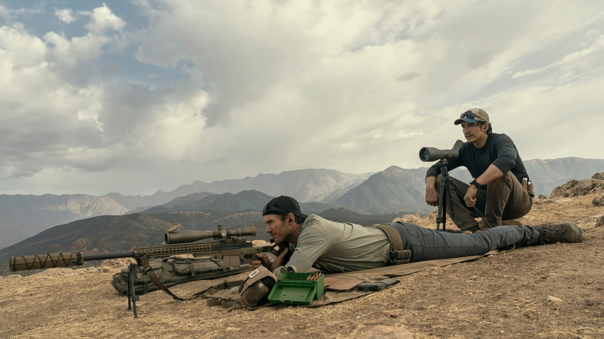 James Reece lies behind a sniper rifle while Freddy Strain sits beside a spotting scope.