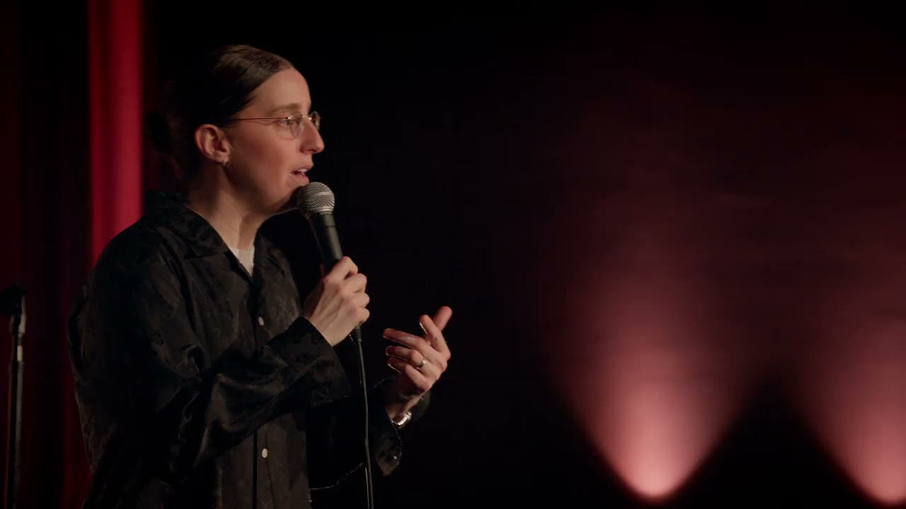 Robby Hoffman speaks in profile on the Wake Up stage, with red curtain and warm floor lights.