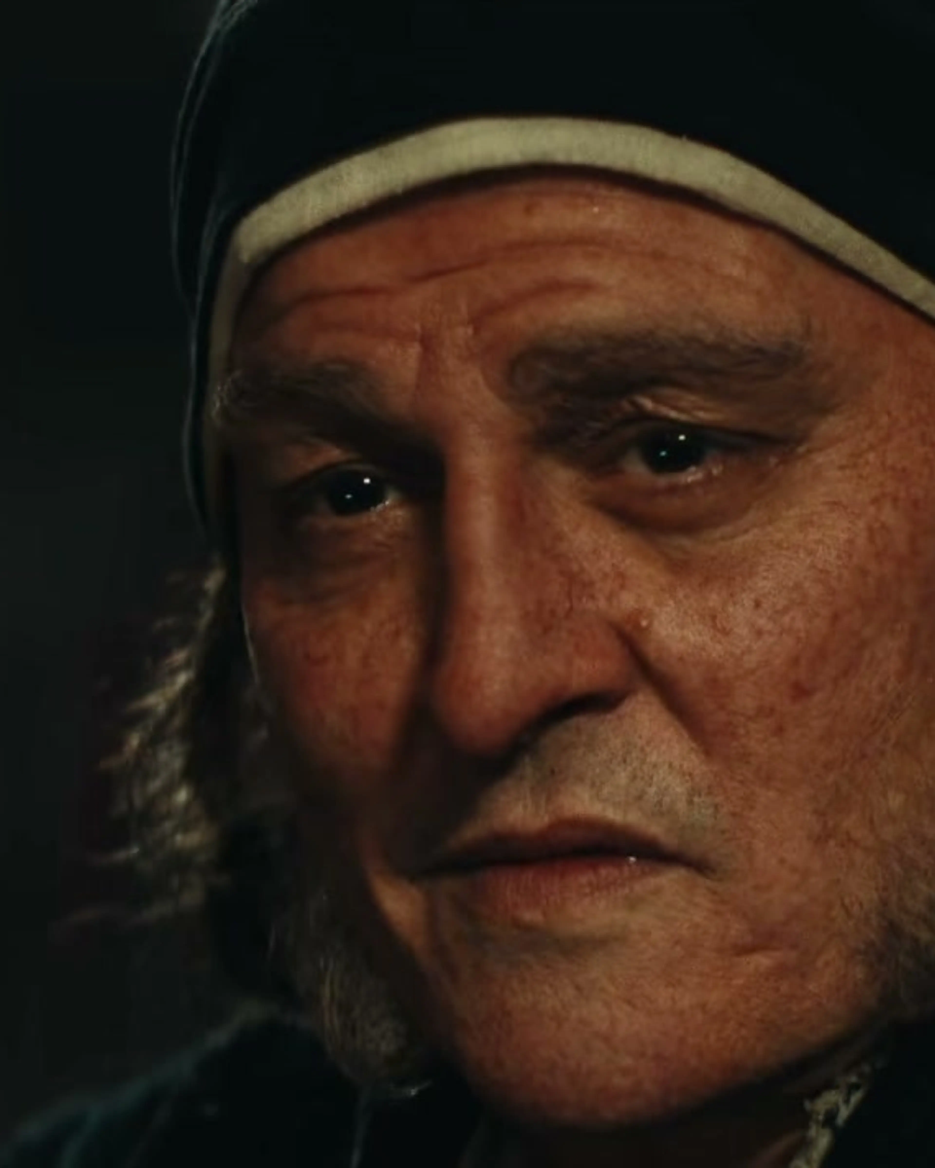 Johnny Depp as Scrooge in a dark cap and coat in Ebenezer.
