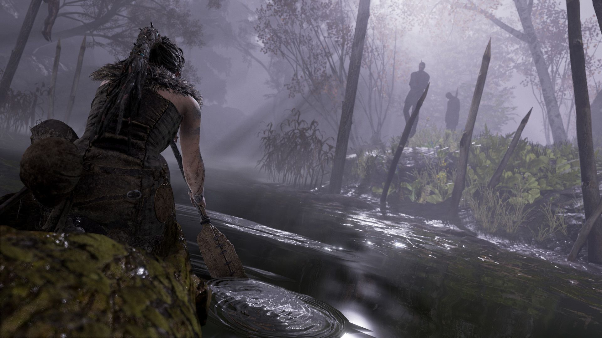 Senua walks through a misty wooded place with figures in the distance.