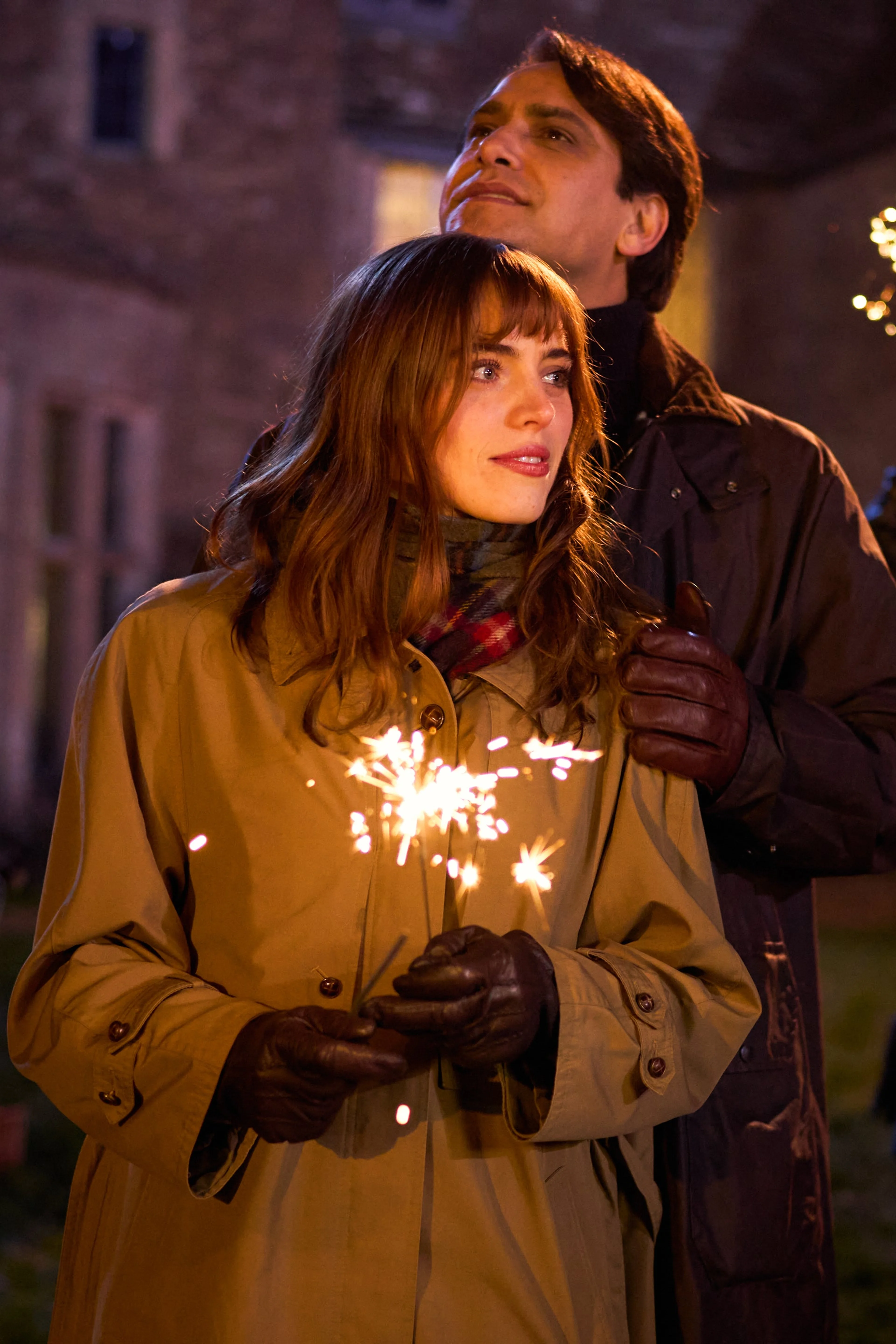 Bella Maclean as Taggie O’Hara holds sparklers with Luca Pasqualino as Bas Baddingham behind her.