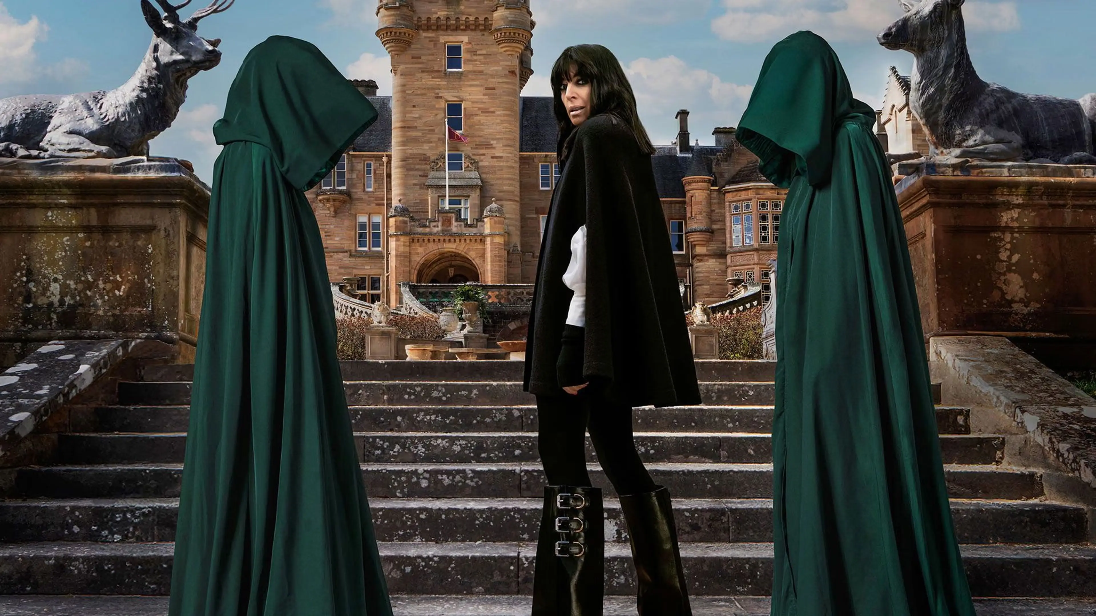 Claudia Winkleman stands on castle steps between two hooded figures for The Celebrity Traitors.