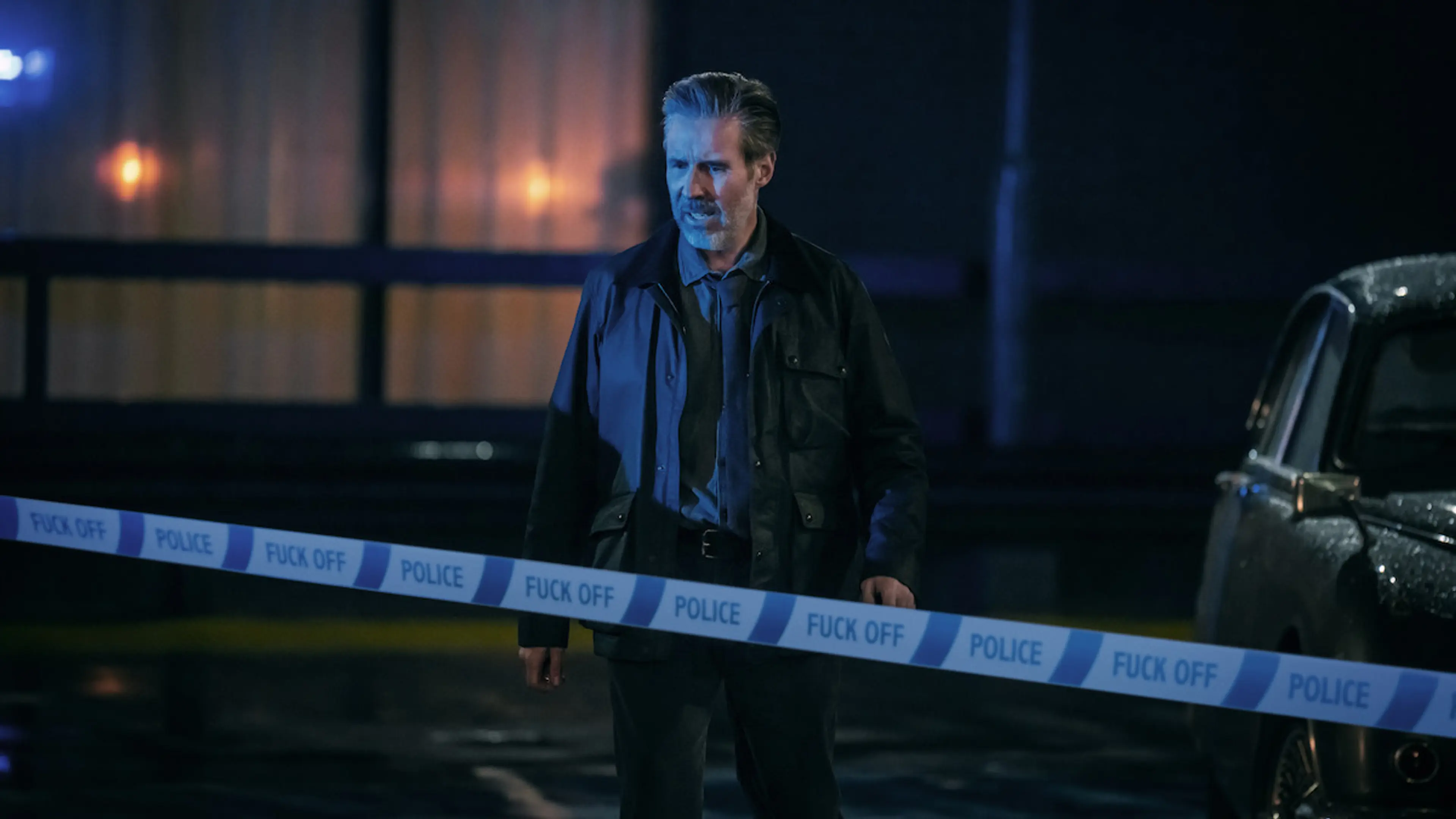 Detective John Blackmere stands behind police tape at a nighttime scene.