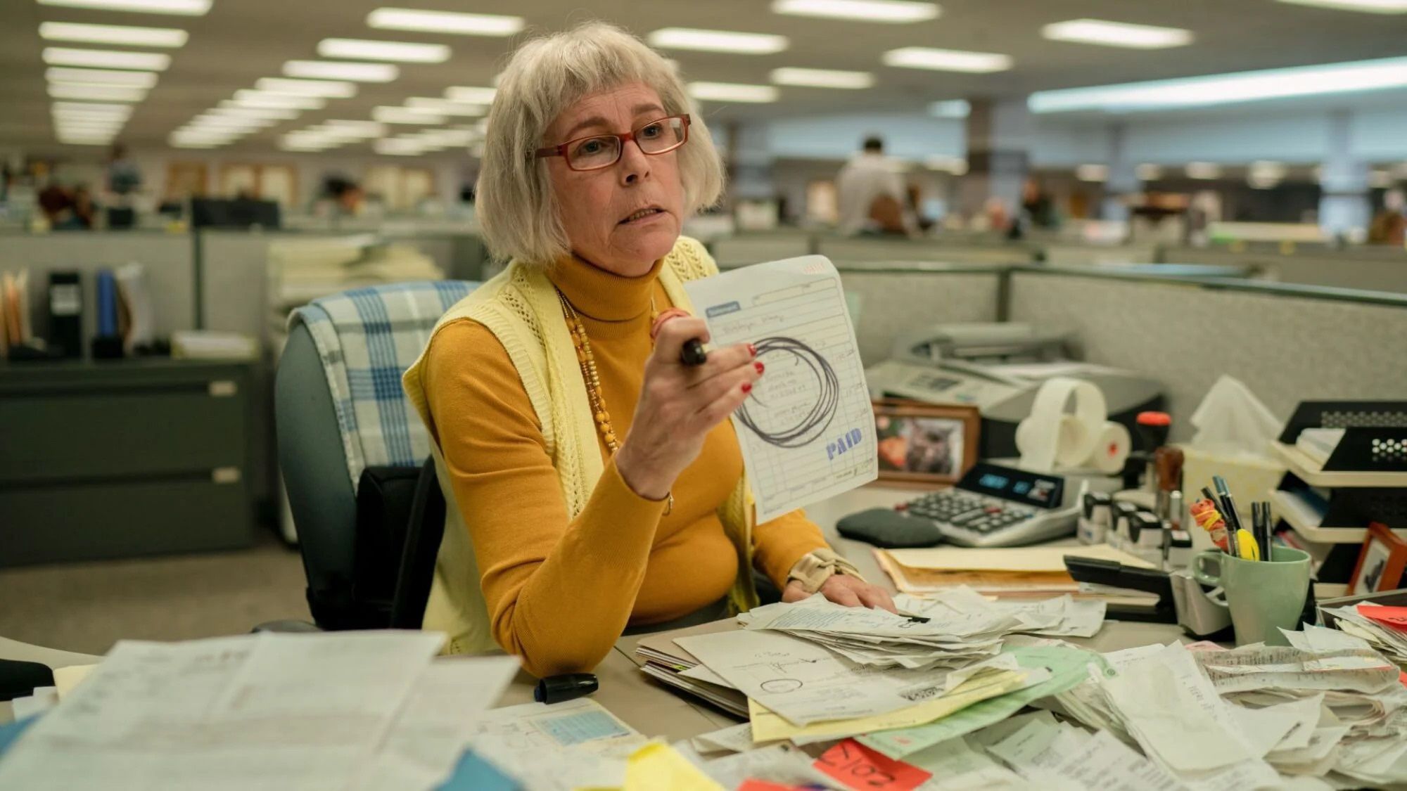 Jamie Lee Curtis sits behind a crowded tax-office desk as Deidre in Everything Everywhere All at Once.