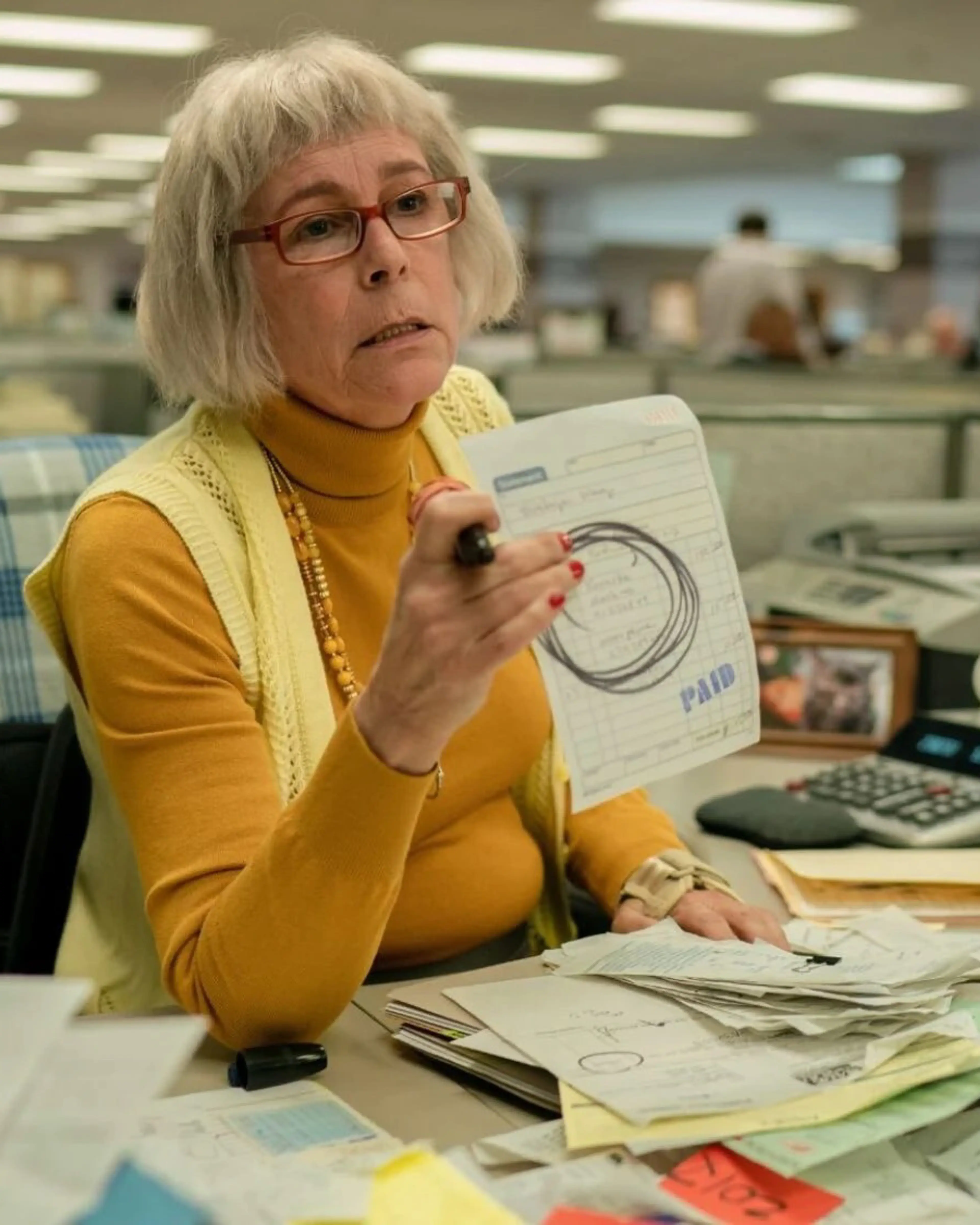 Jamie Lee Curtis sits behind a crowded tax-office desk as Deidre in Everything Everywhere All at Once.