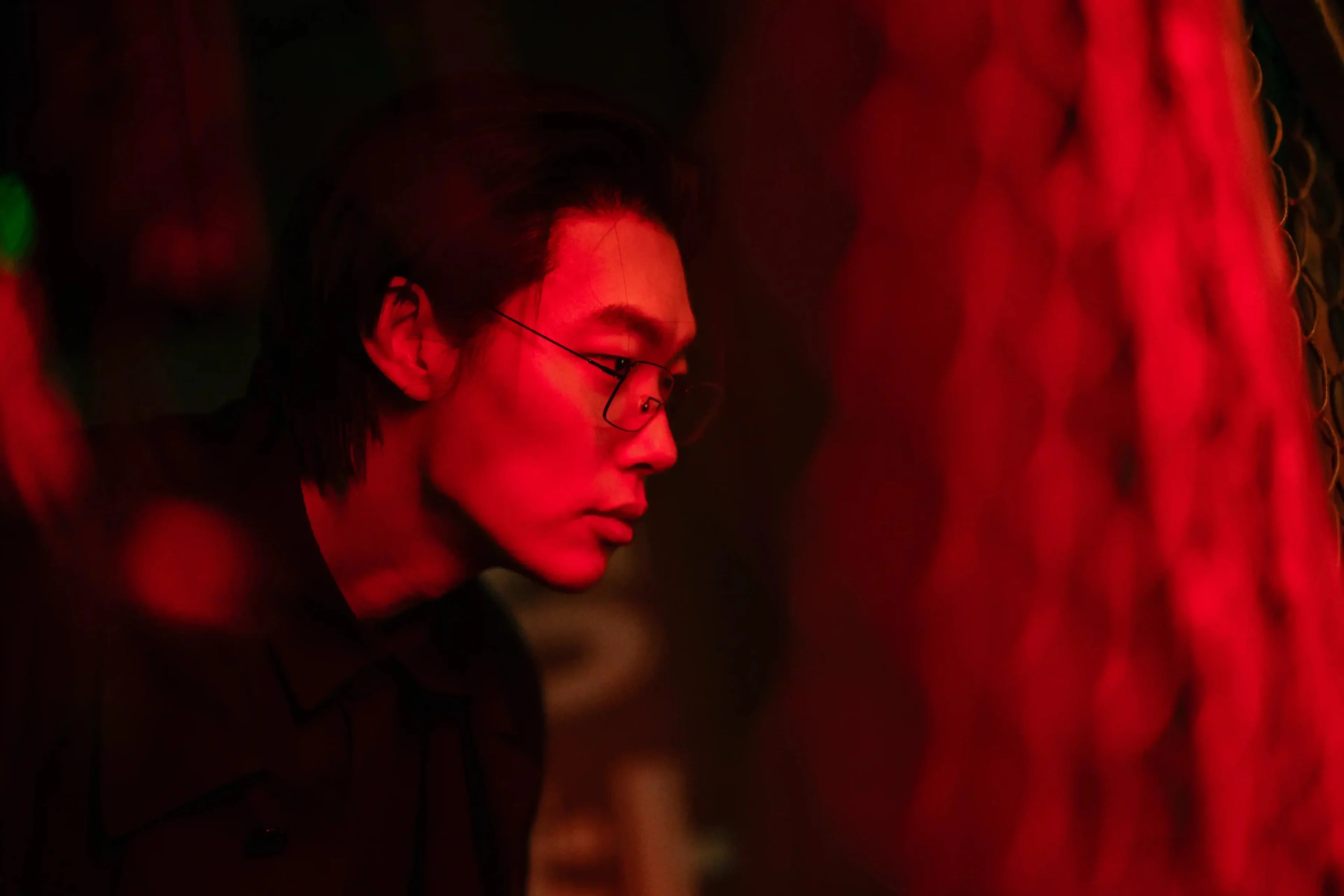 Ryu Jun-yeol wears round glasses beside a tree in red light.