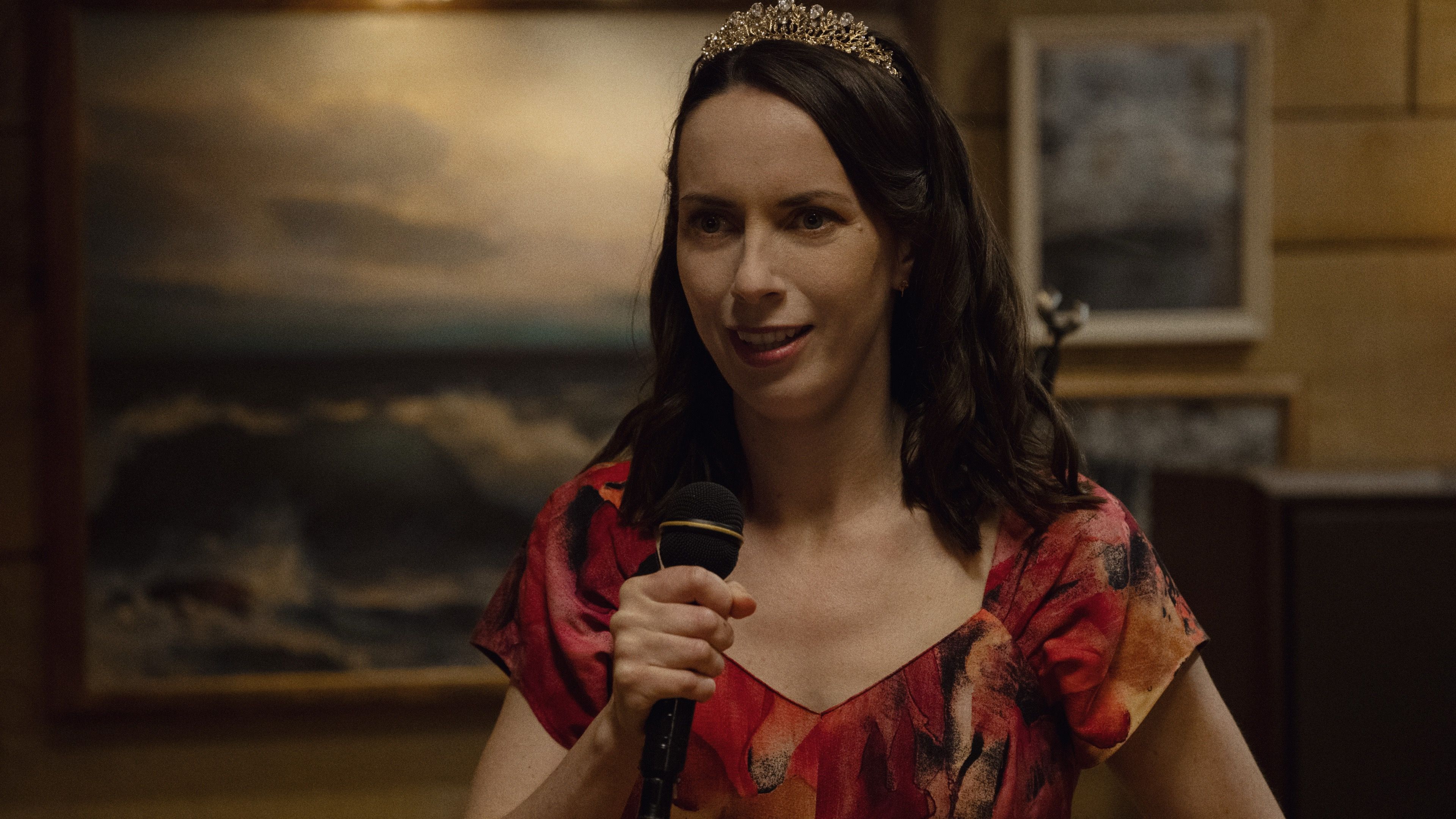 Kate O’Flynn as Patricia holds a microphone and wears a tiara during a night out.