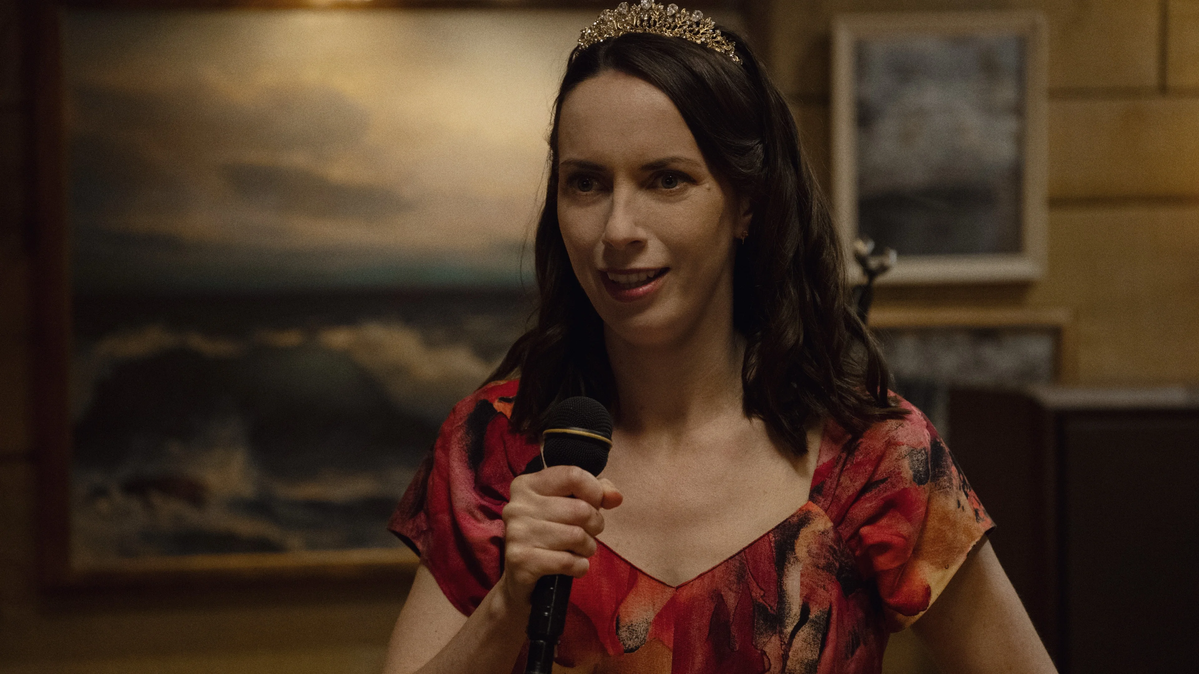 Kate O’Flynn as Patricia holds a microphone and wears a tiara during a night out.