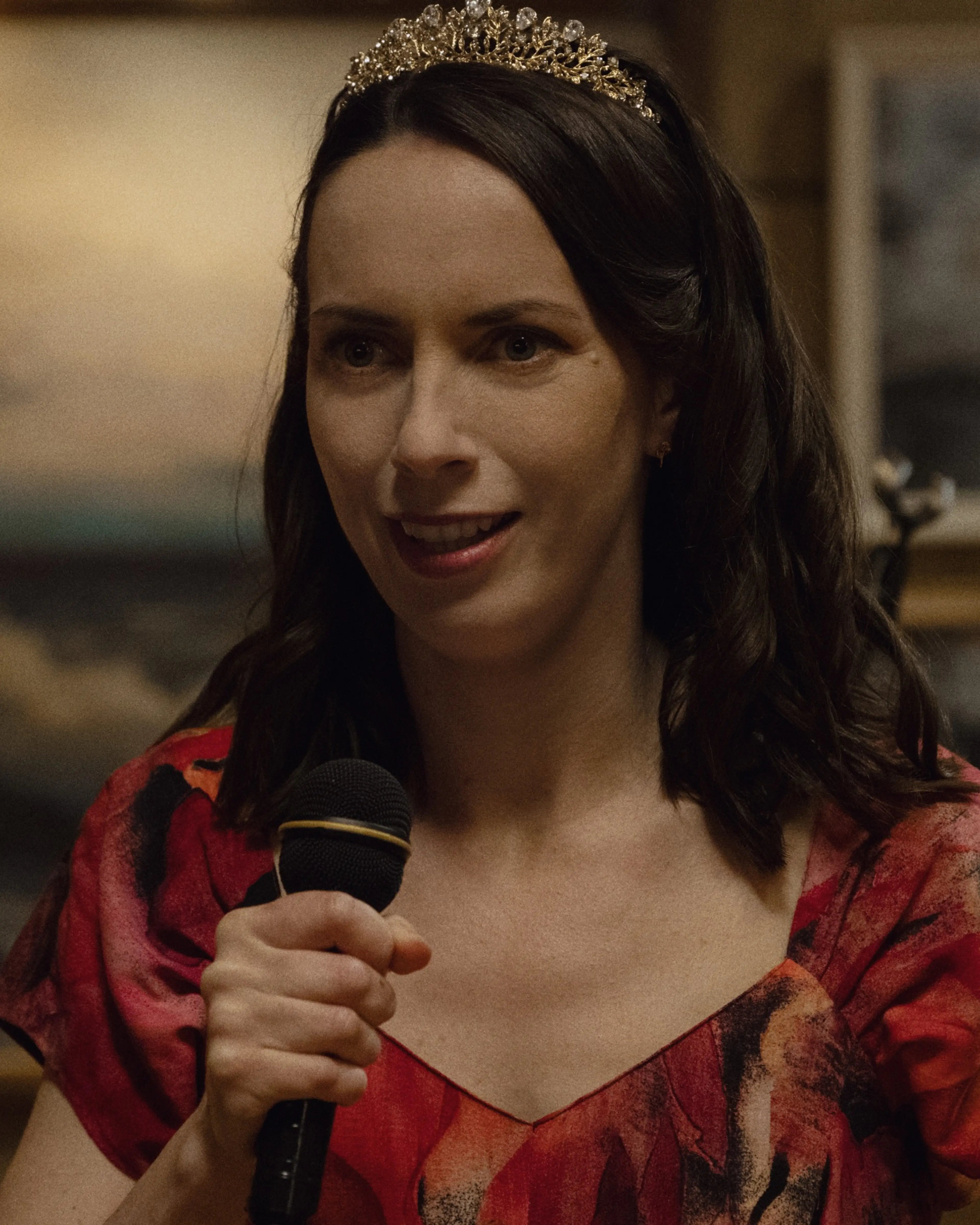 Kate O’Flynn as Patricia holds a microphone and wears a tiara during a night out.