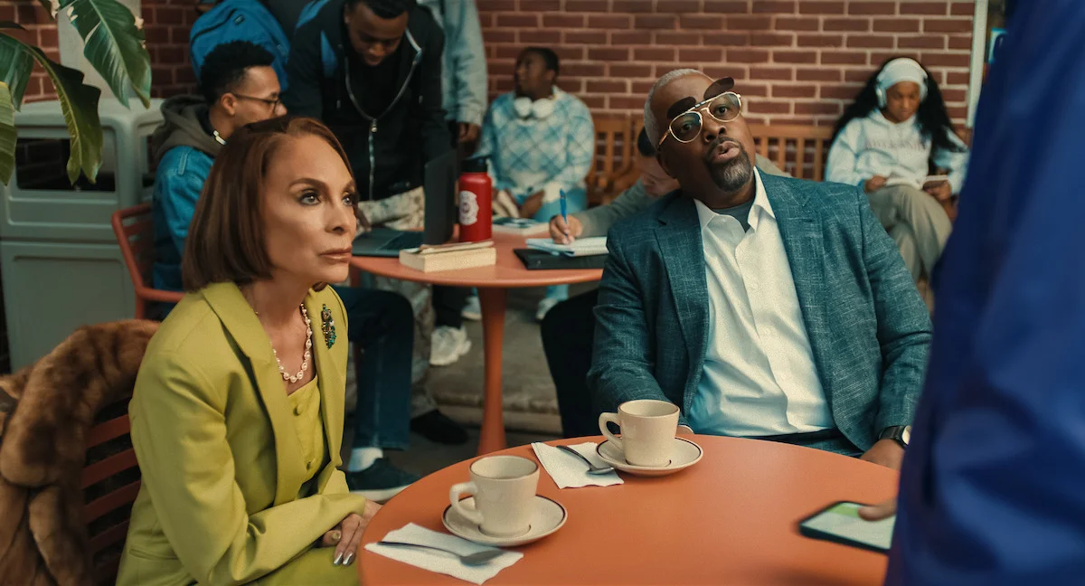 Jasmine Guy as Whitley and Kadeem Hardison as Dwayne sit at a café table with coffee cups, looking toward someone standing beside them.