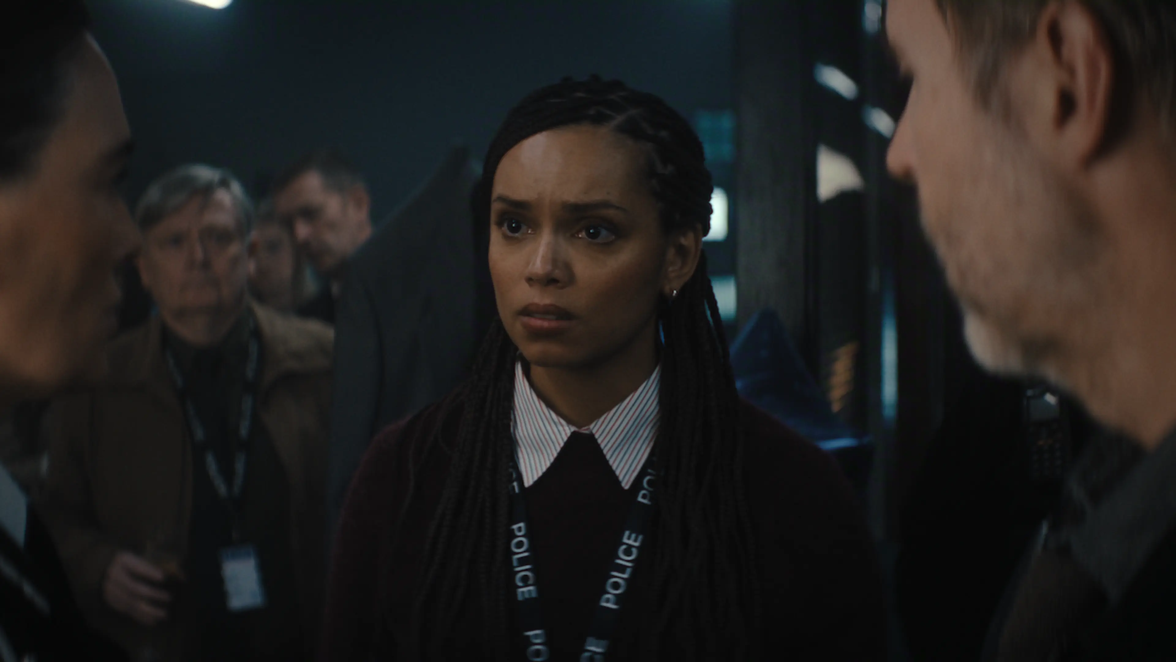 A woman wearing a police lanyard stands among colleagues in a busy station.