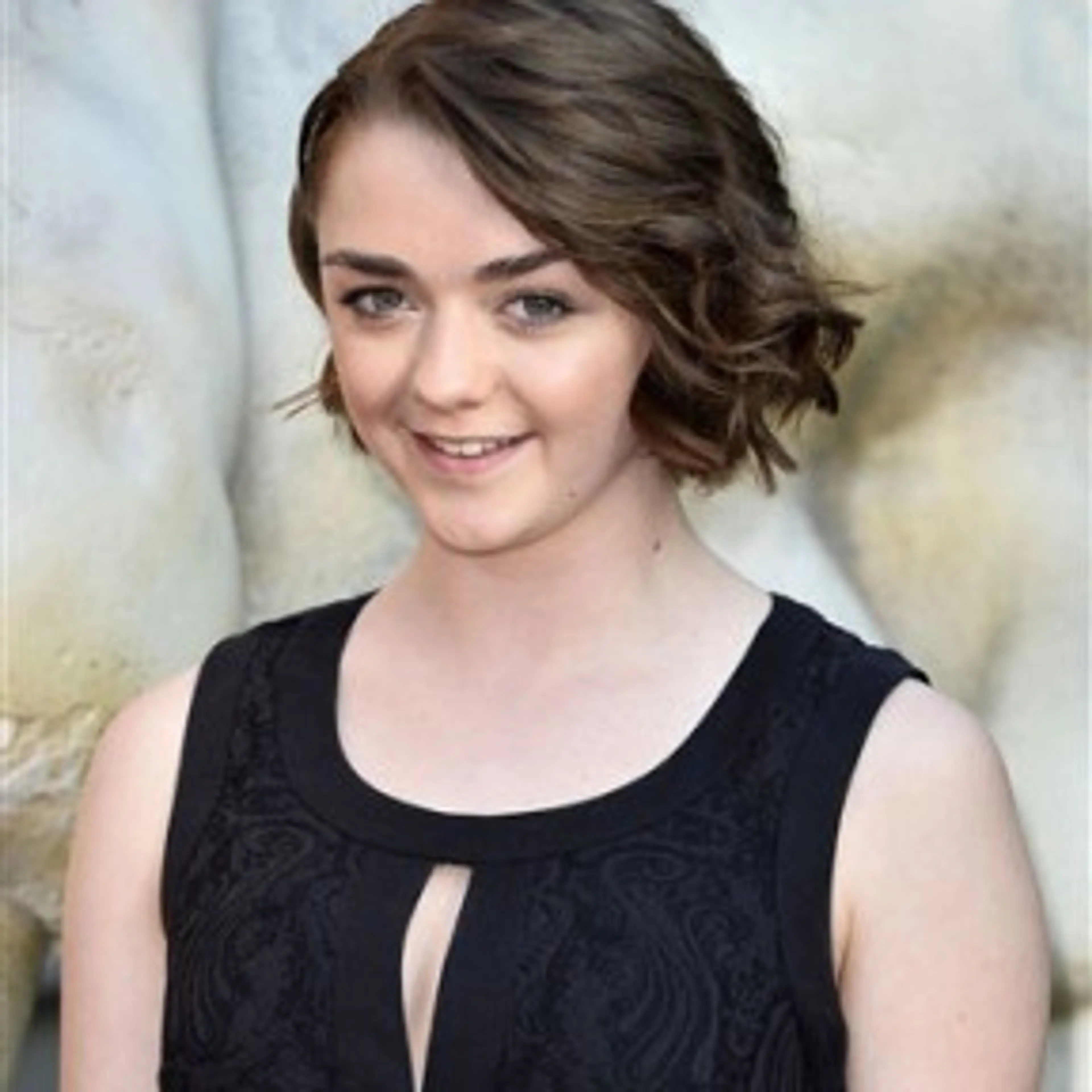 Portrait of Maisie Williams smiling in a black sleeveless dress.