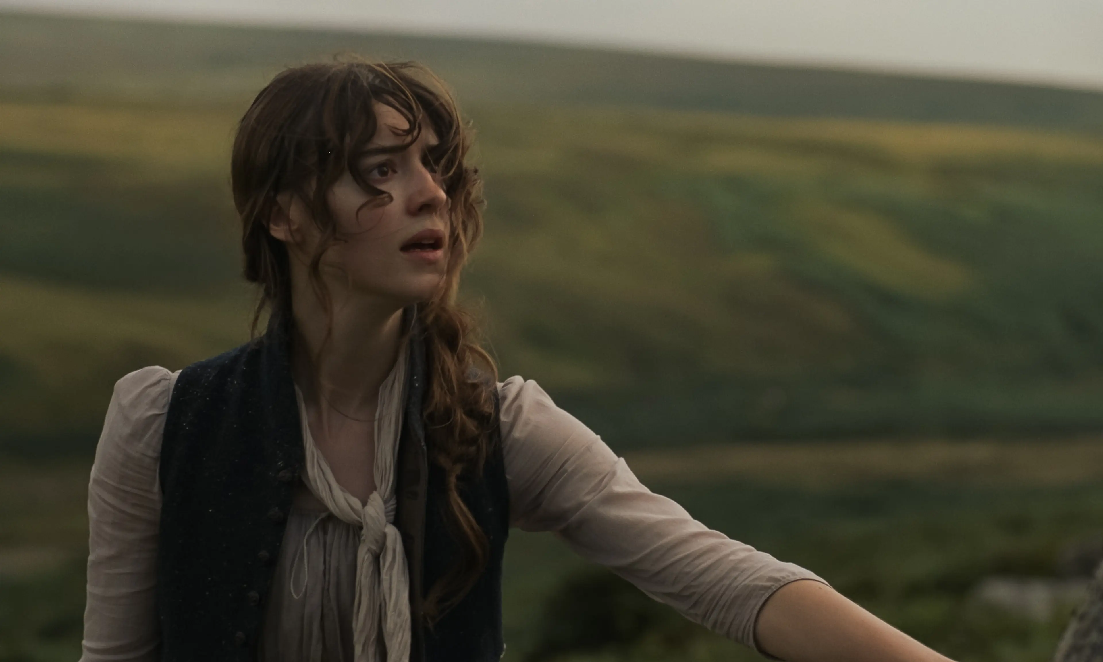 Elinor stands outdoors in a pale dress and dark waistcoat.