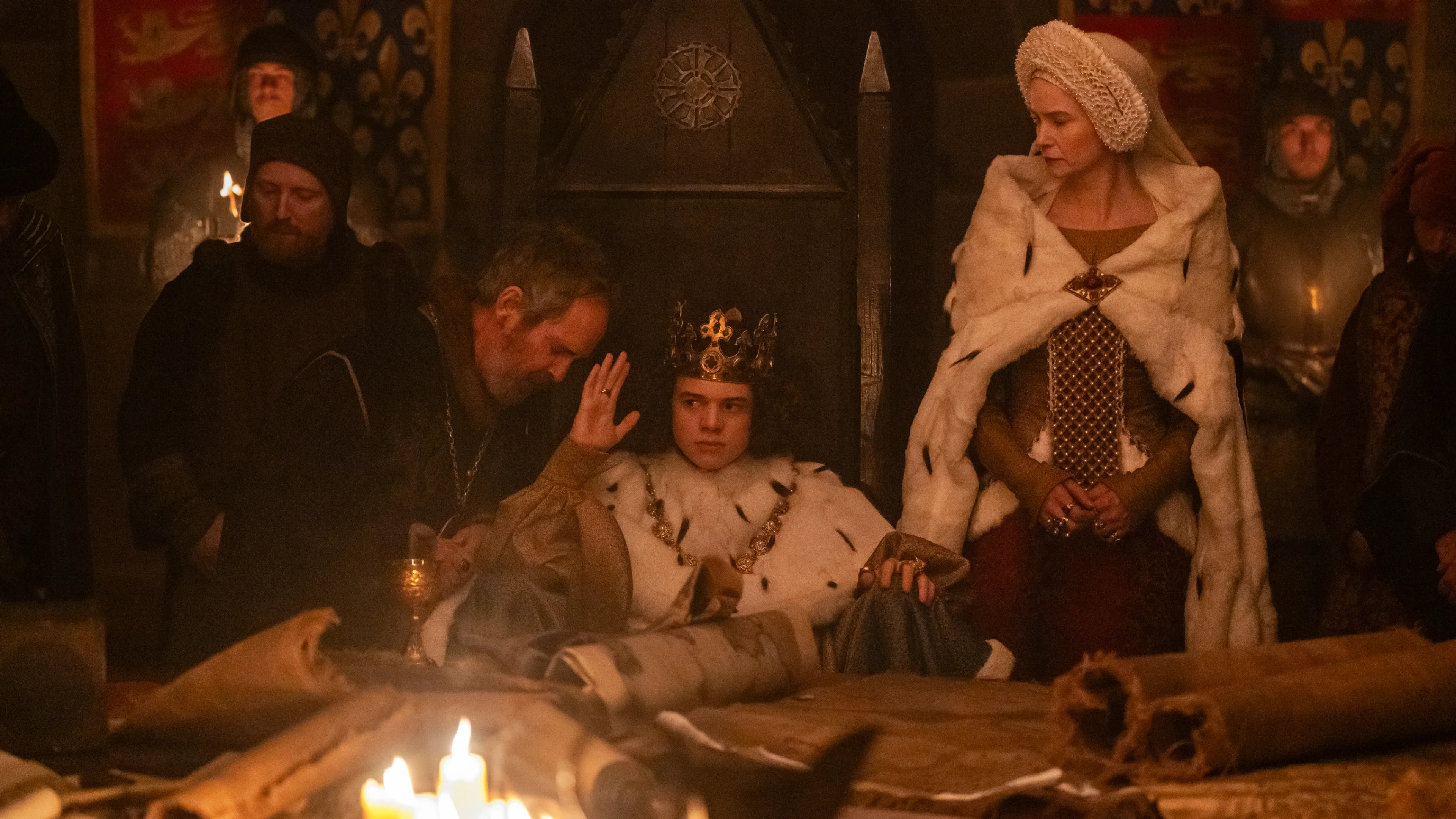 Tom Hollander leans toward Woody Norman on the throne as Katherine Waterston watches.