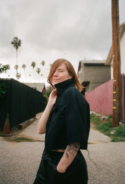 Erin Lee Carr stands outdoors, looking back toward the camera.