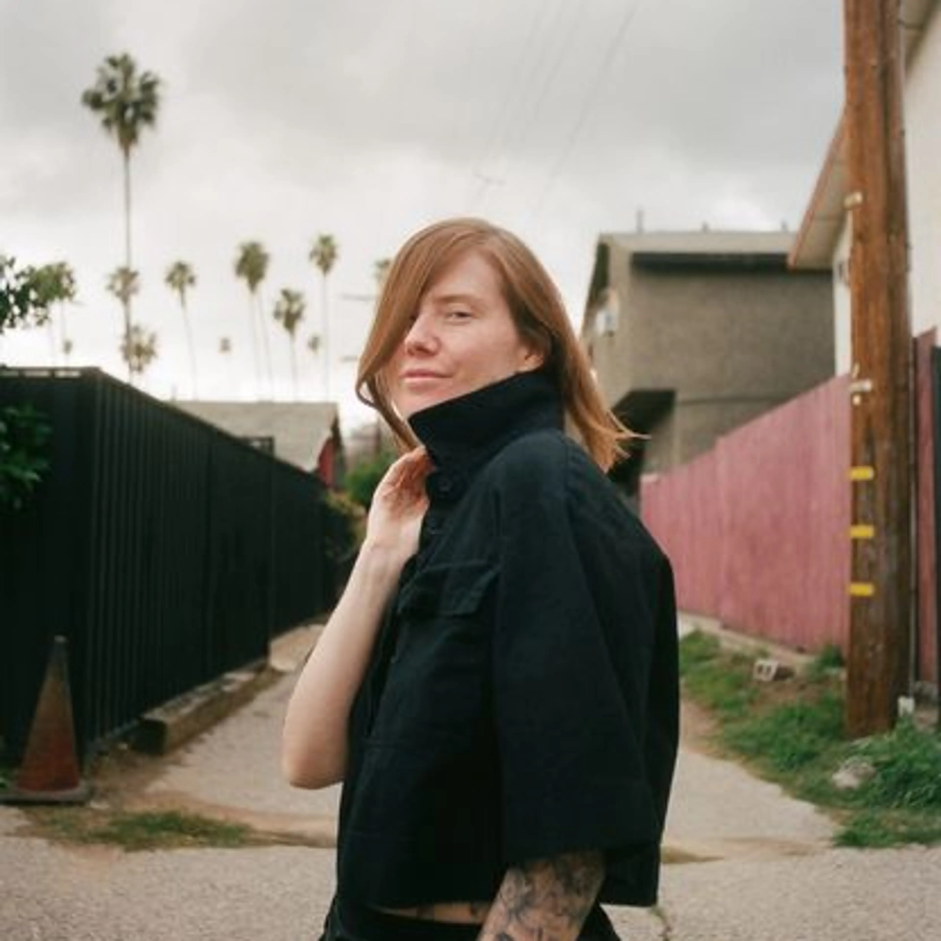 Erin Lee Carr stands outdoors, looking back toward the camera.