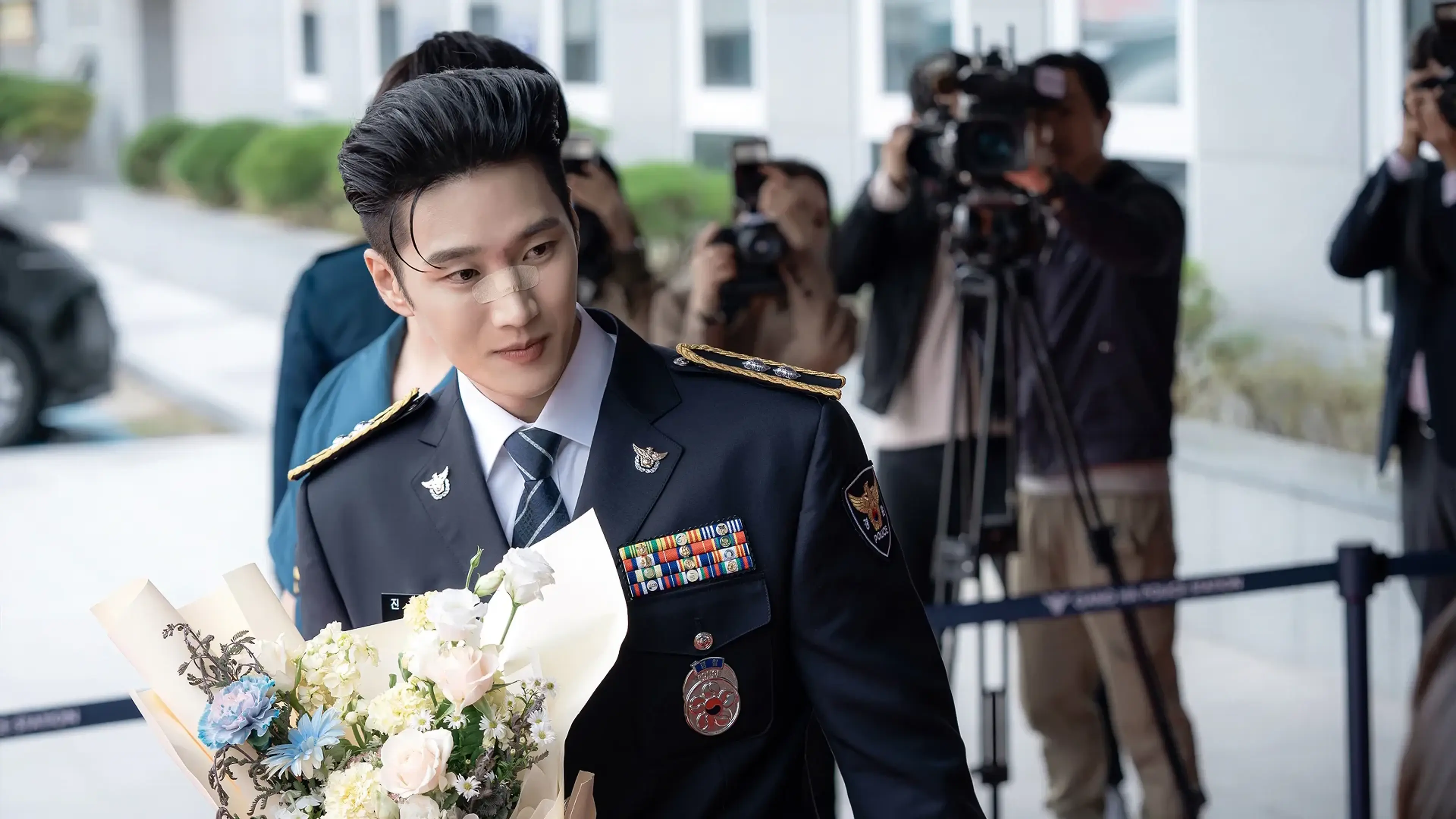 Jin I-soo wears his police uniform while holding flowers in front of photographers.