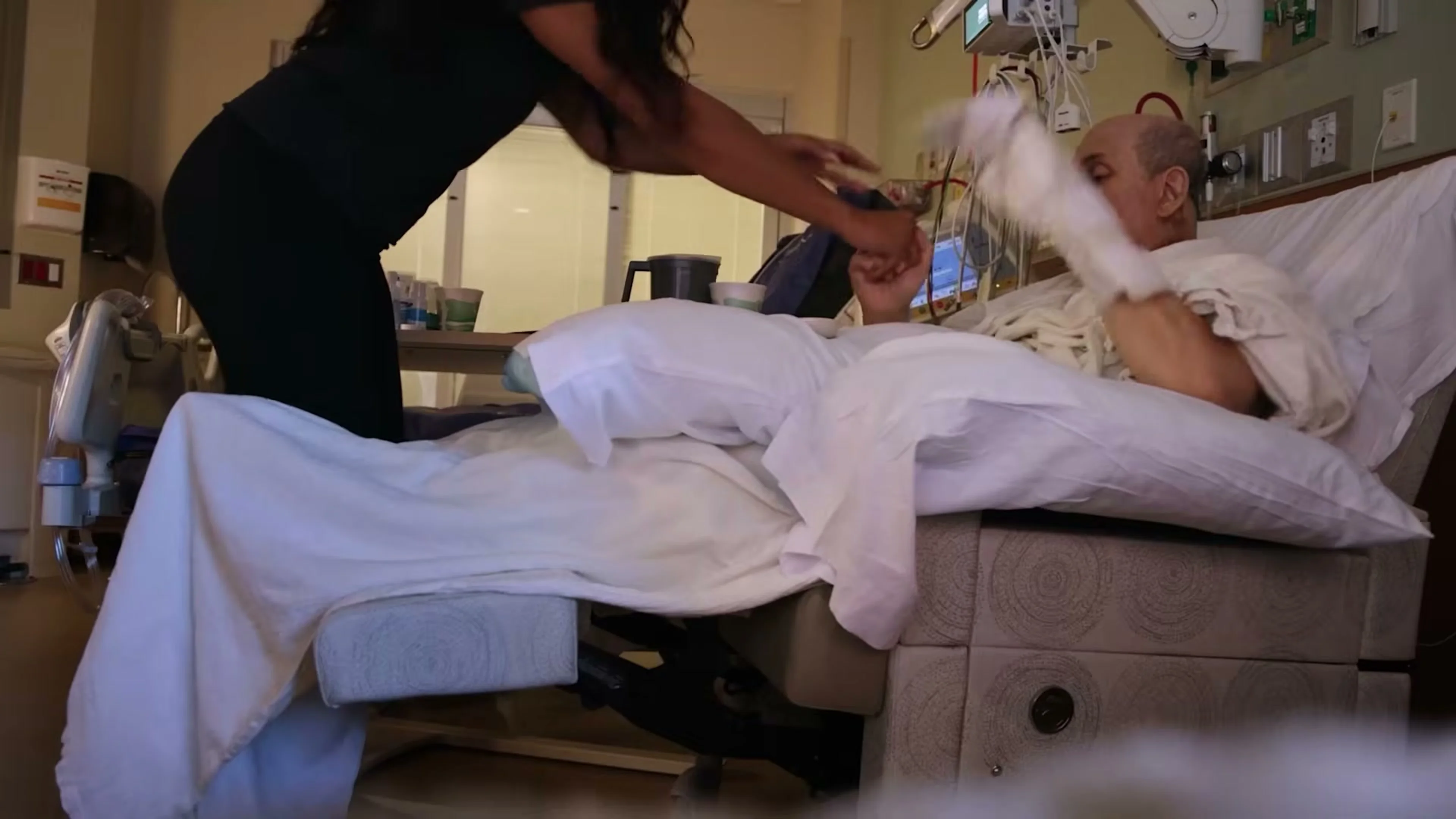 Salman Rushdie raises his arms during rehabilitation in a hospital room.