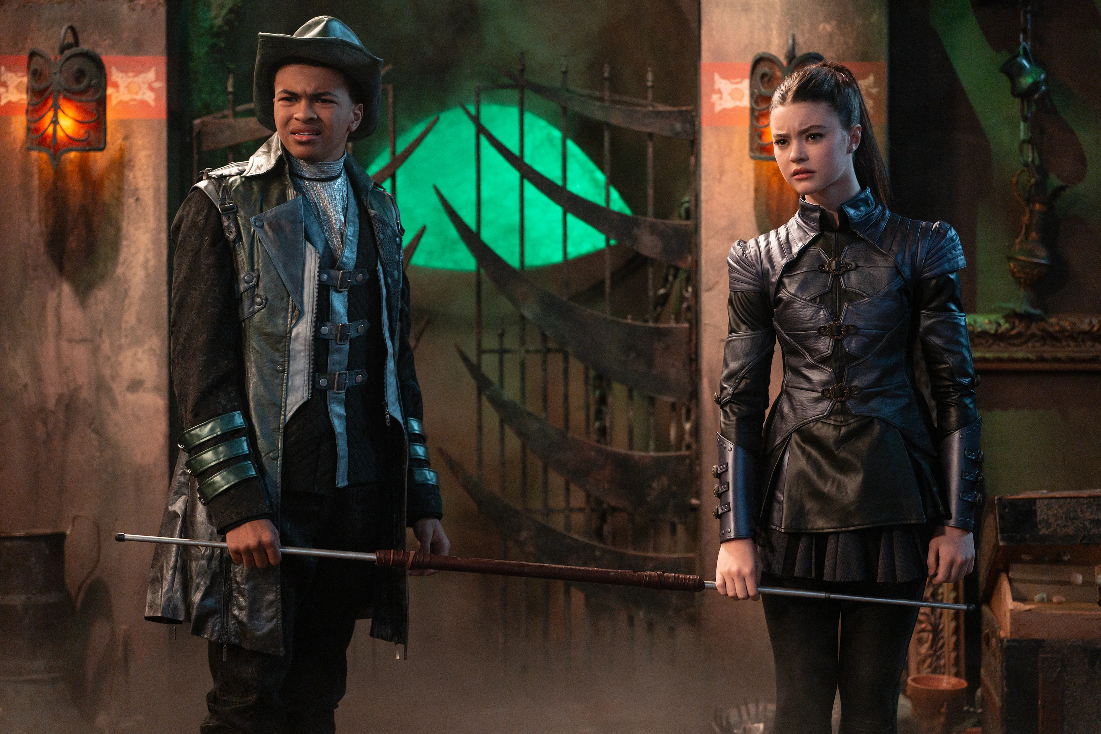 Shaun Dixon as Elijah and Kenzi Richardson as Vee stand in dark fantasy costumes inside a green-lit chamber in Vampirina Season 2.