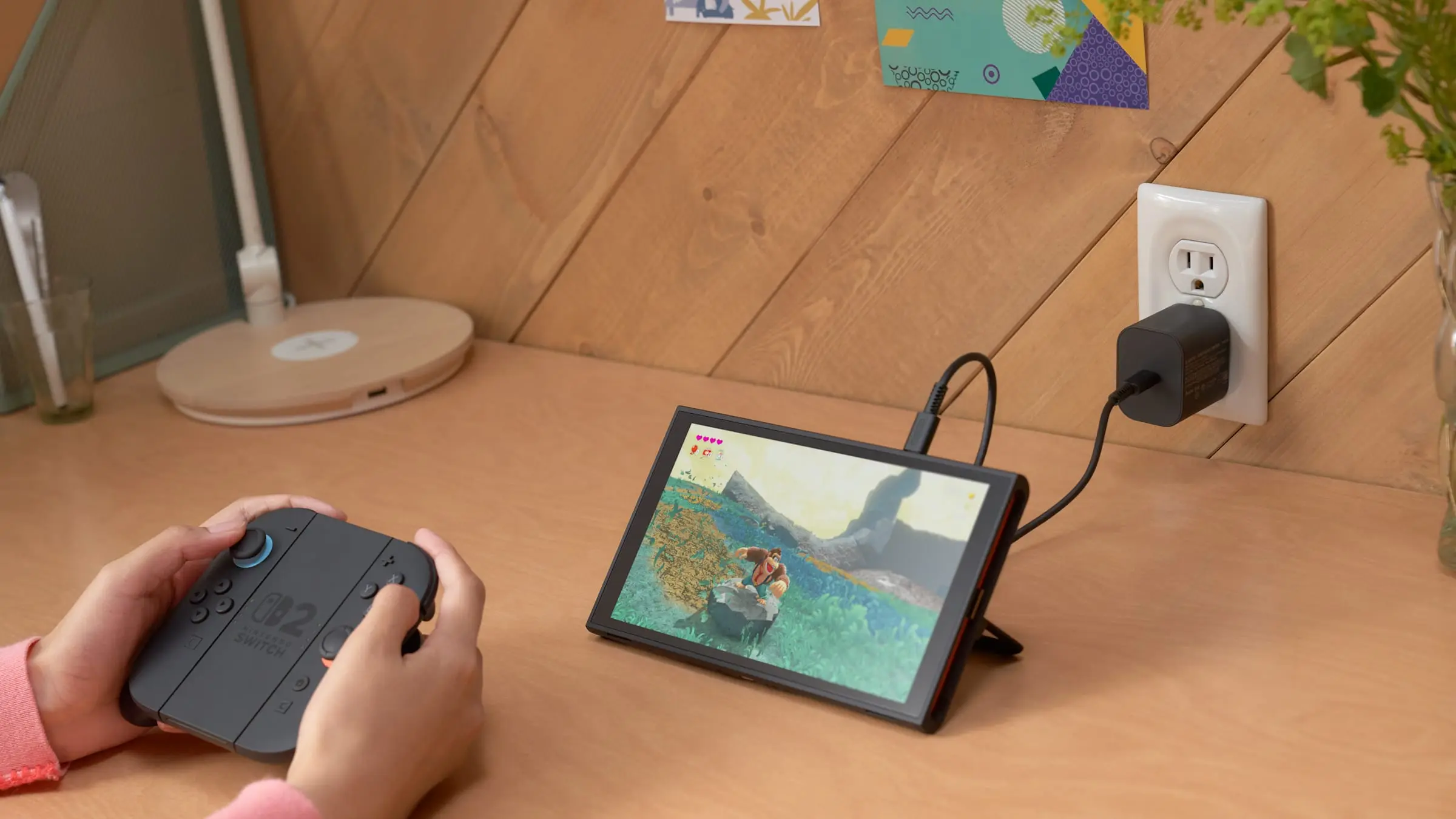 A person plays Nintendo Switch 2 in tabletop mode while the system charges on a desk.