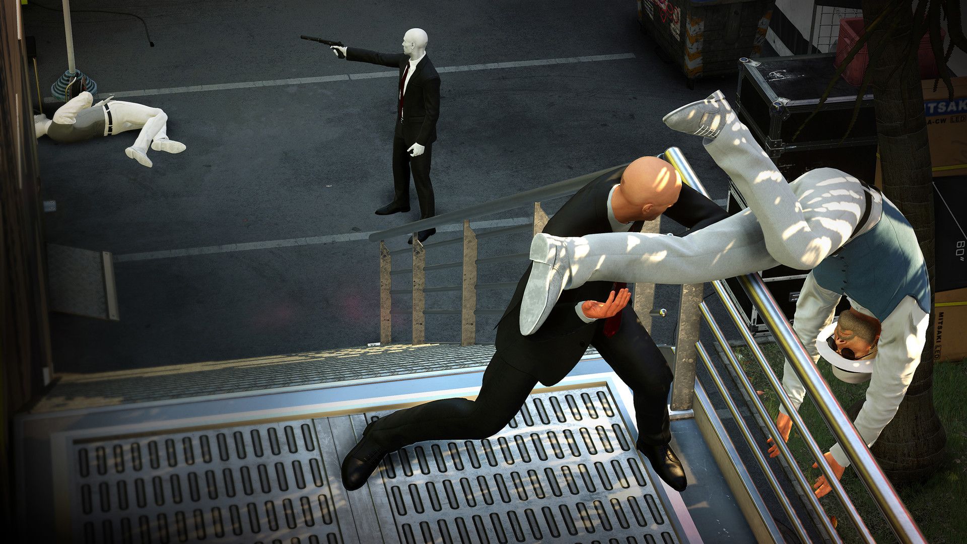 Agent 47 grapples with a person on stairs above a street.
