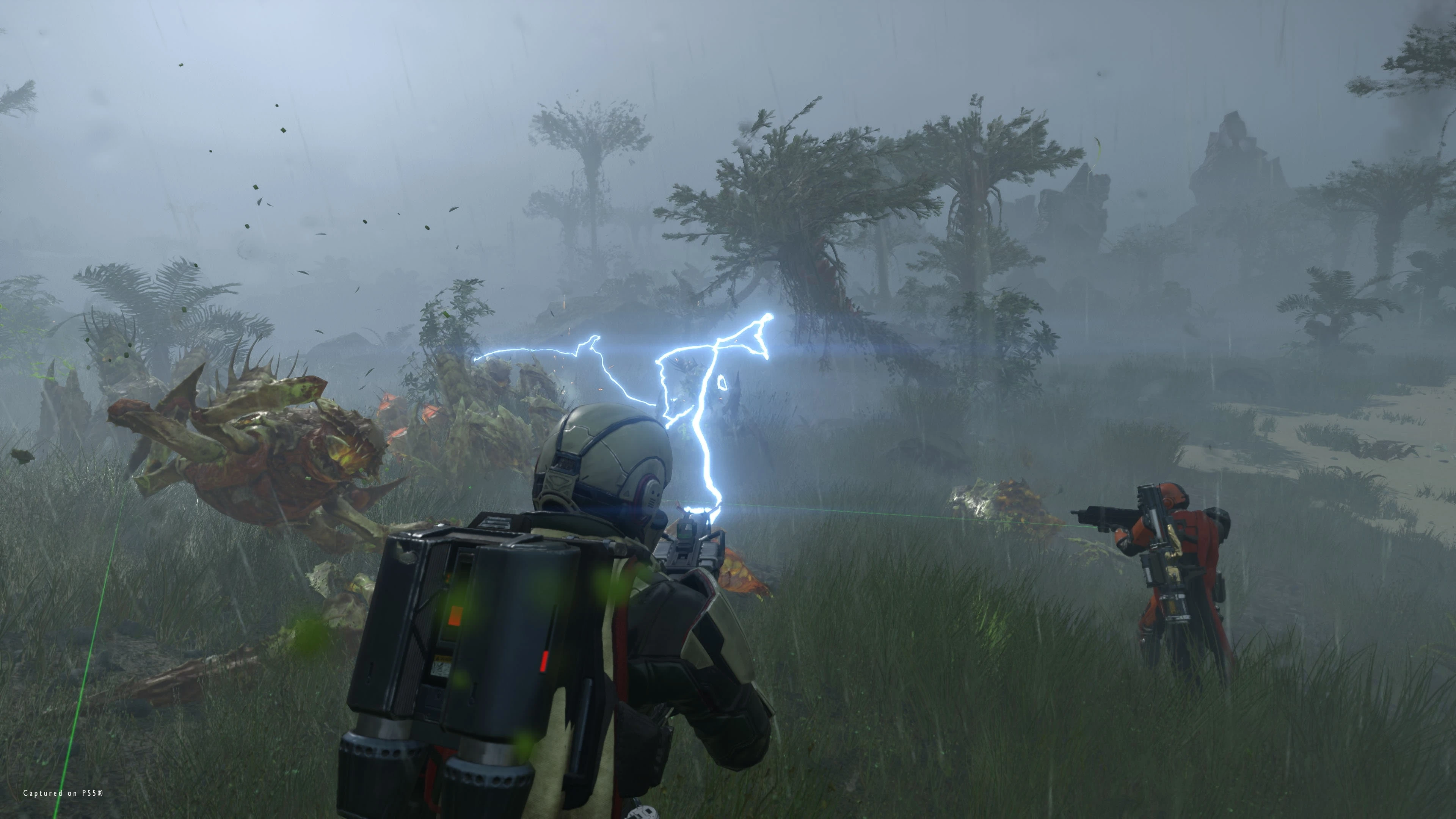 A Helldiver with a support backpack faces Terminids while two squadmates provide fire on a stormy alien world.