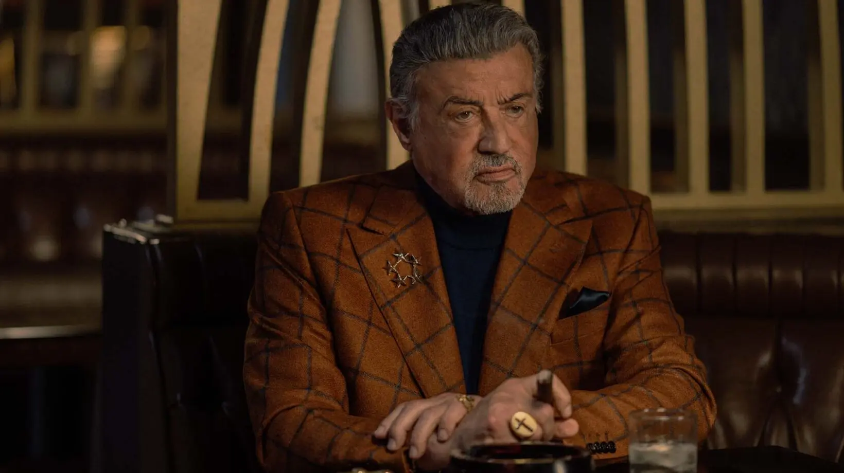 Sylvester Stallone as Dwight Manfredi sits in a dim restaurant in Tulsa King Season 4.