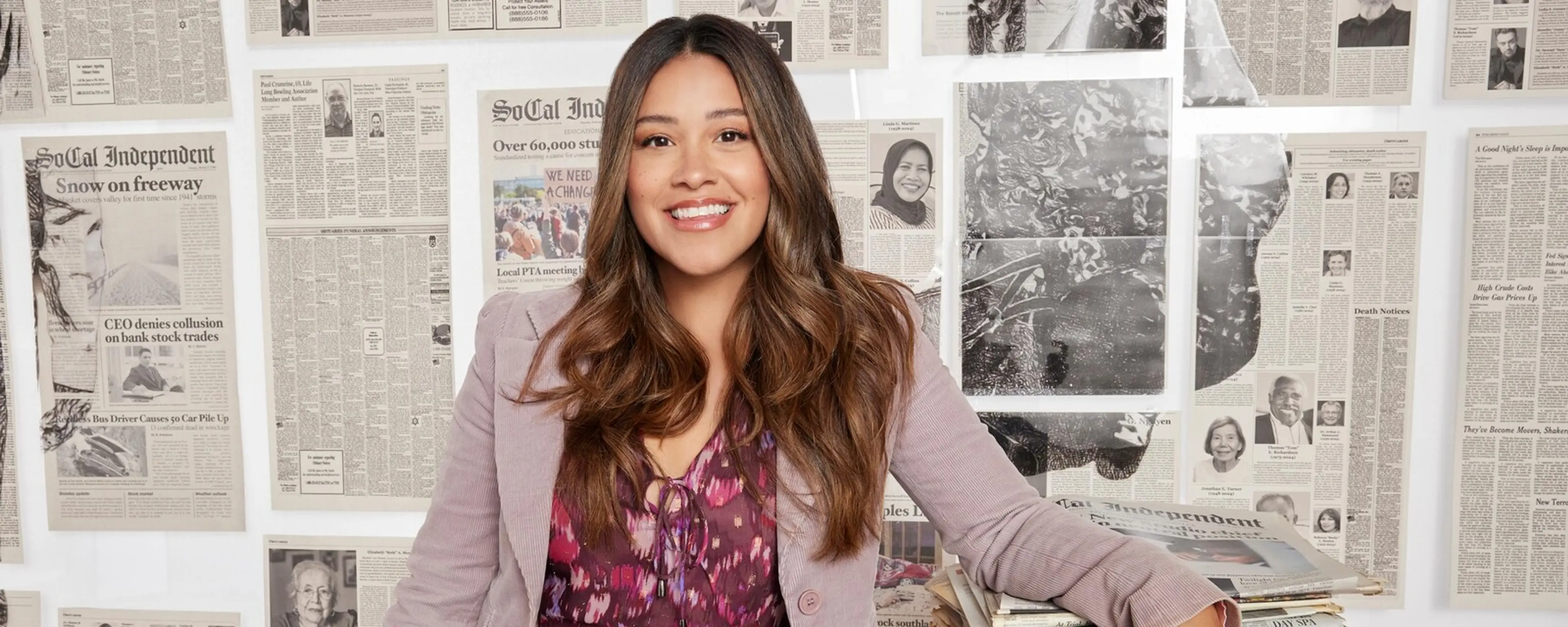 Gina Rodriguez smiles in an ABC promotional portrait for Not Dead Yet, with newspapers behind her.