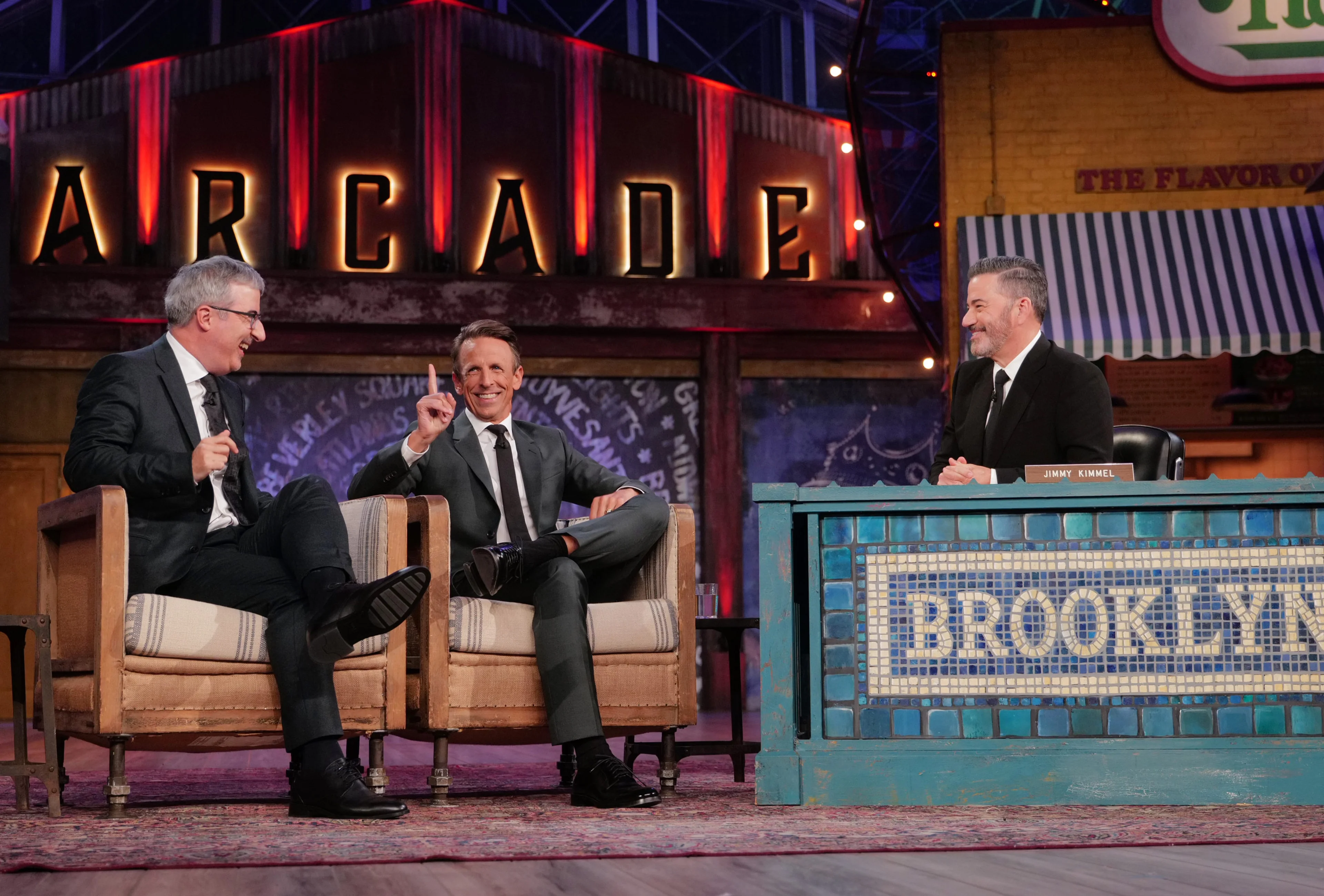 Seth Meyers raises a finger between John Oliver on the left and Jimmy Kimmel on the right.