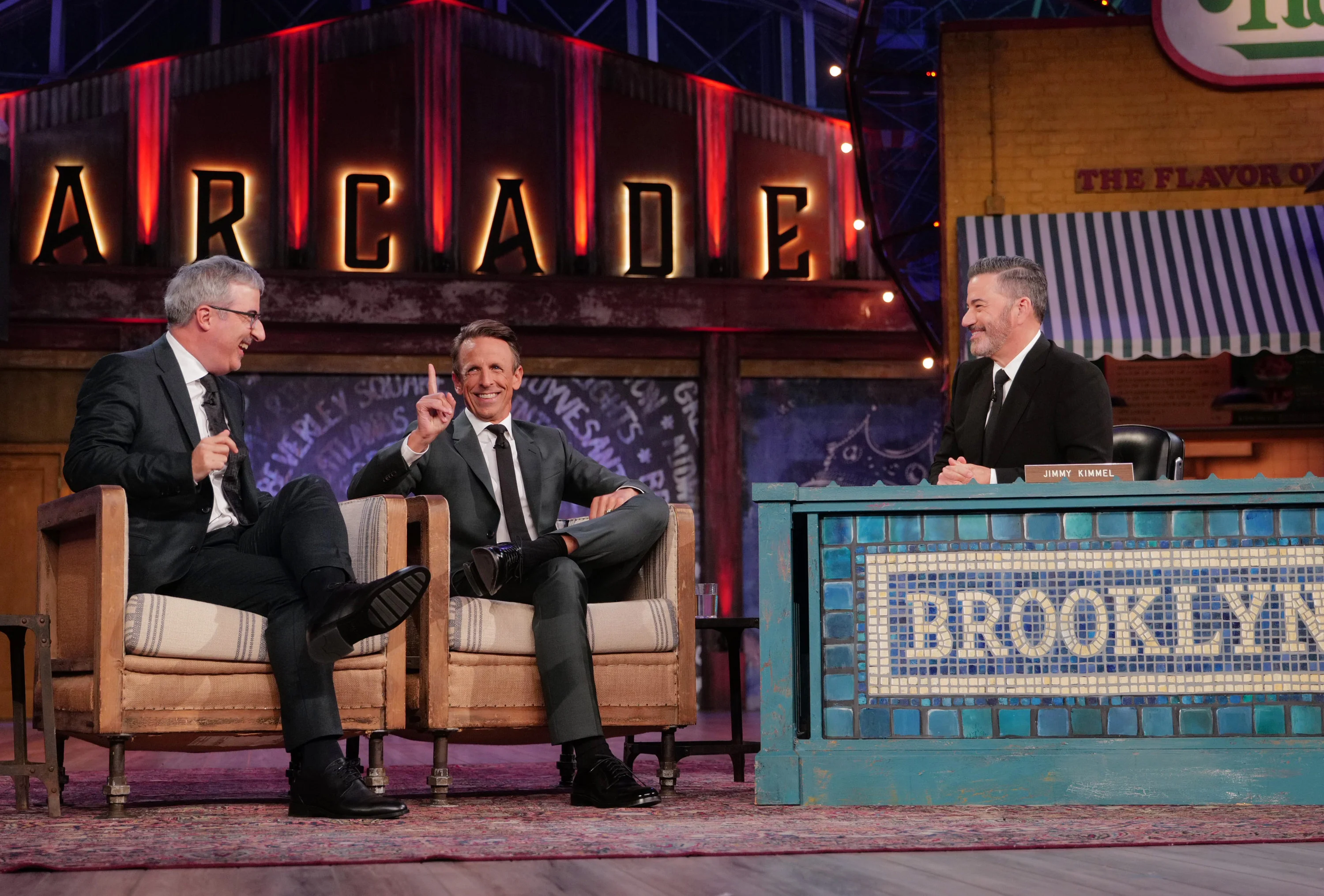 Seth Meyers raises a finger between John Oliver on the left and Jimmy Kimmel on the right.