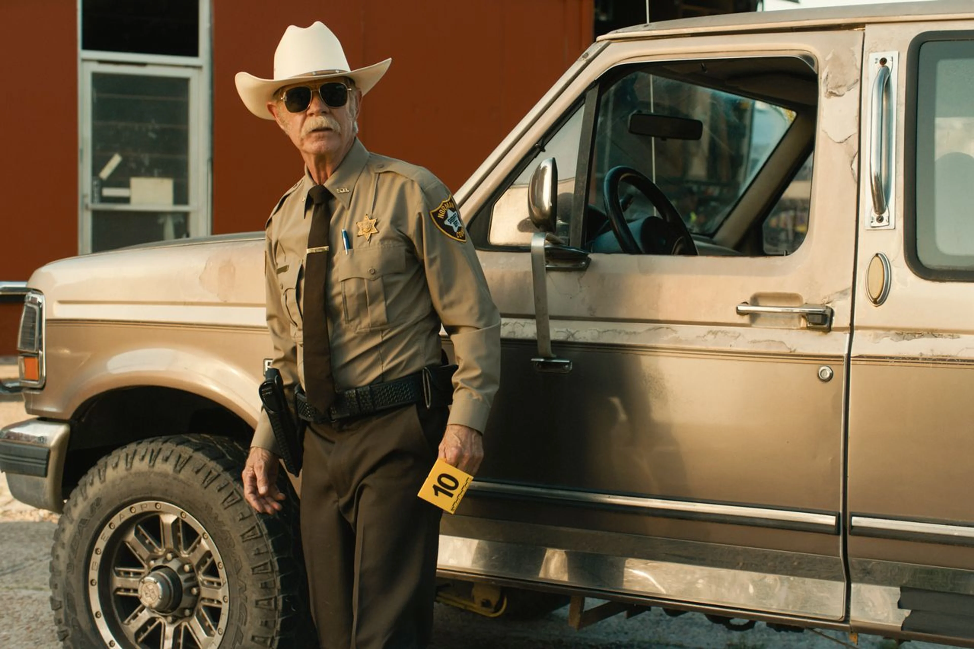 William H. Macy stands by a sheriff’s truck in a scene from The Deputy.