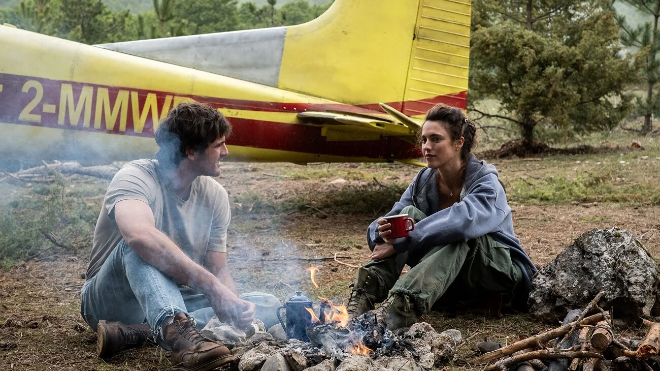 Jacob Elordi as Hig and Margaret Qualley as Cima sit beside a campfire and yellow plane in The Dog Stars.