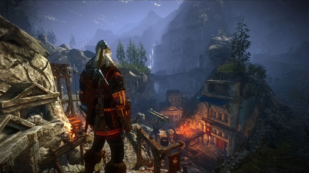 Geralt looks over a settlement among rocky mountain slopes in The Witcher 2 Enhanced Edition.