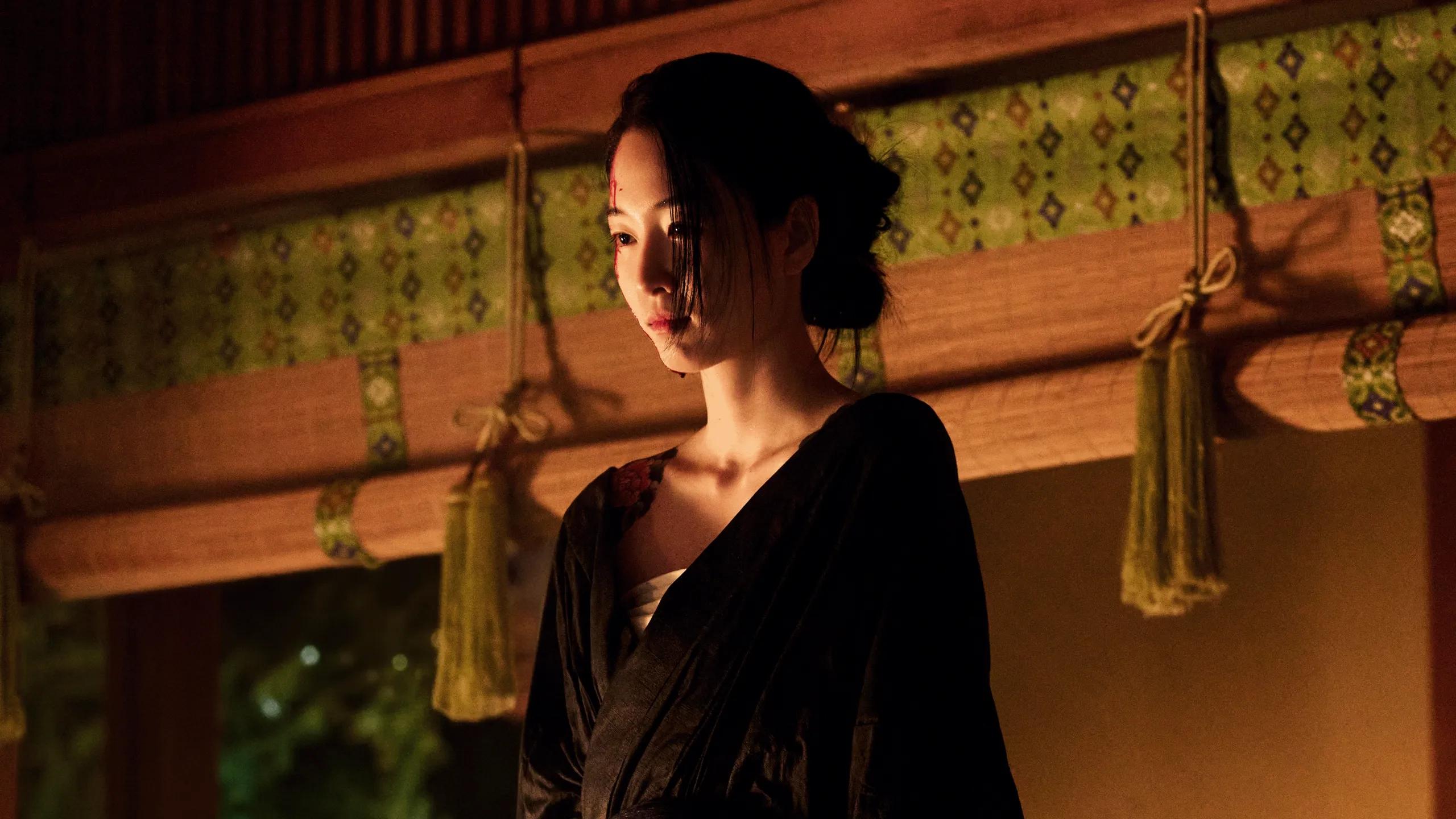 Won Ji-an as Yuji wears a dark robe in a warmly lit wood-paneled room.