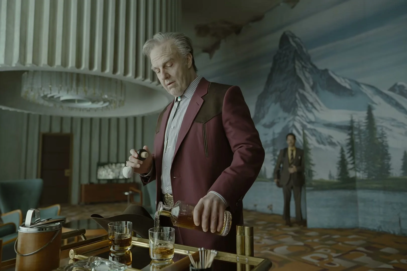 Tom Cruise as Digger Rockwell pours a drink in a room decorated with a mountain mural.