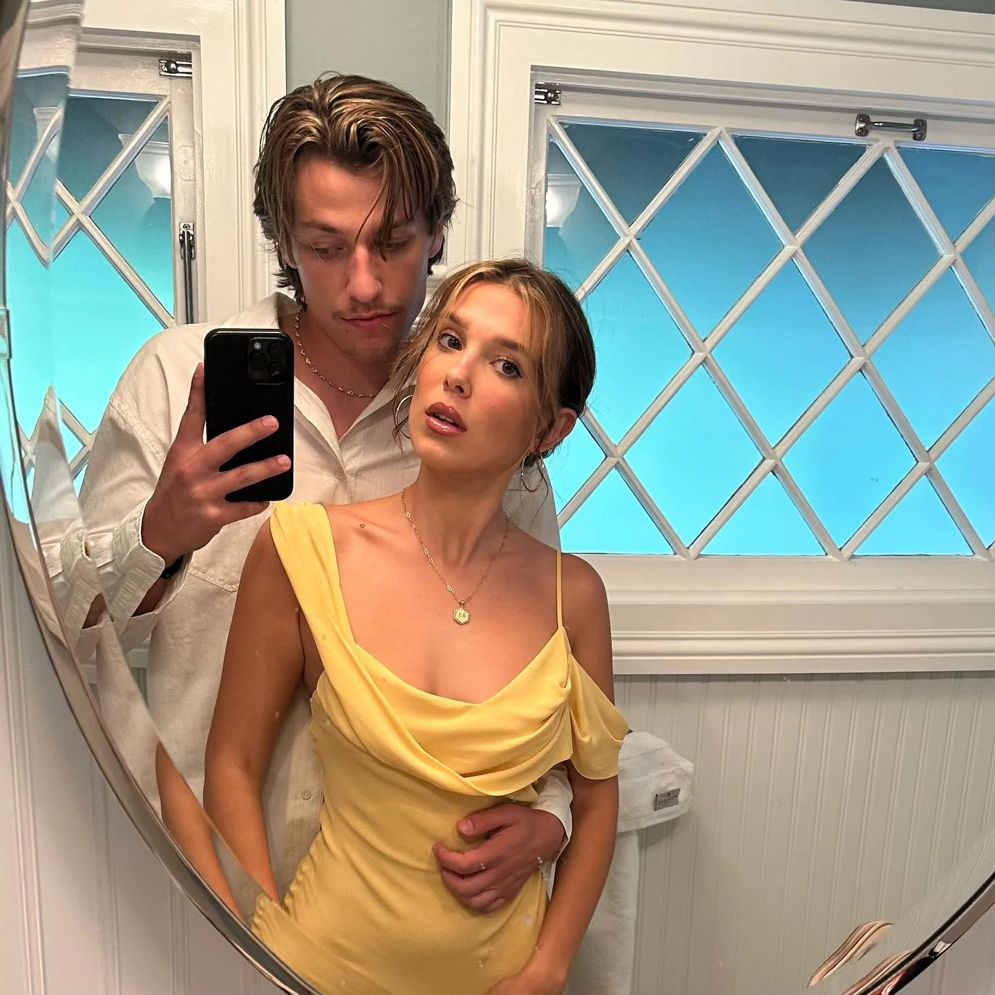 Jake Bongiovi and Millie Bobby Brown posing for a mirror selfie; Brown wears a yellow dress.
