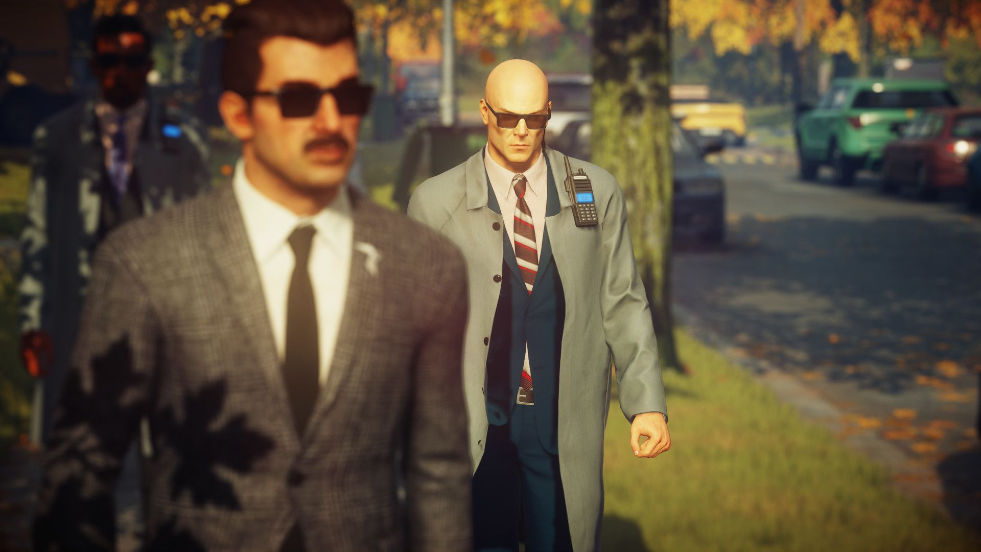 Agent 47 walks behind another suited man in a residential street.