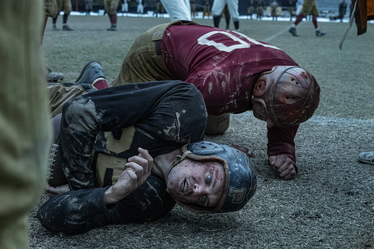 Ray Nicholson as Tony Butkovich lies on a muddy football field beside another player in The Mosquito Bowl.