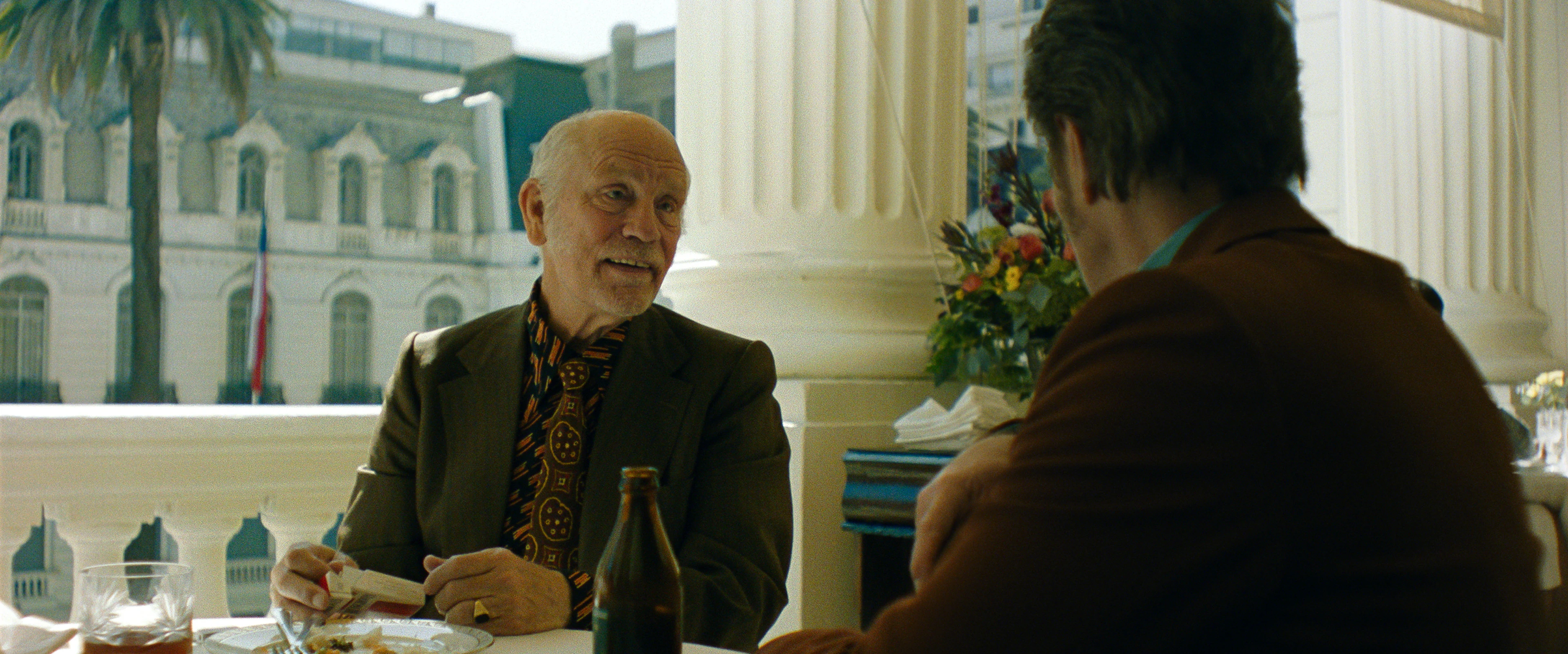 John Malkovich sits at a café table in Wild Horse Nine.