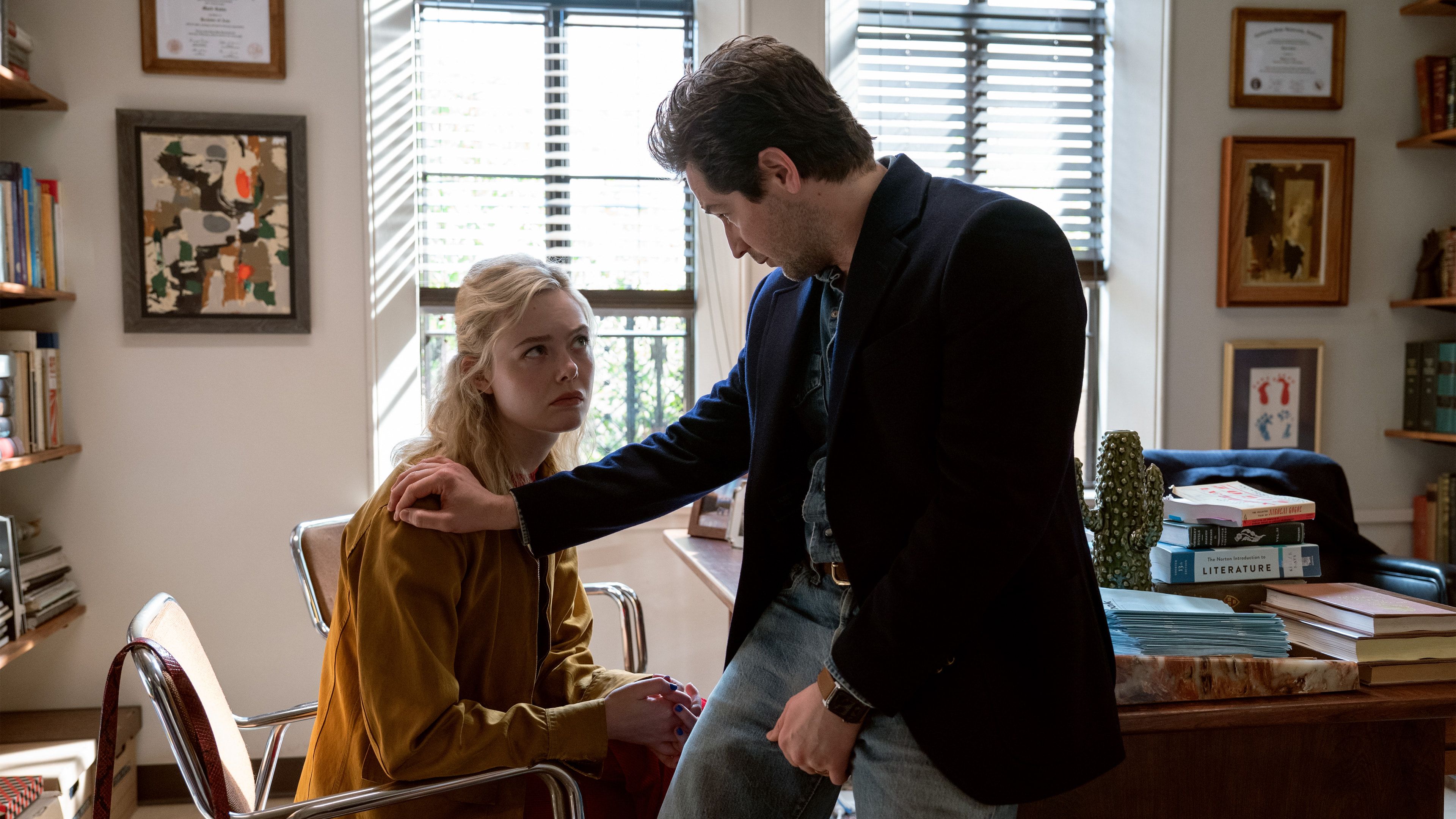 Elle Fanning as Margo sits in an office while Michael Angarano as Mark stands beside her.