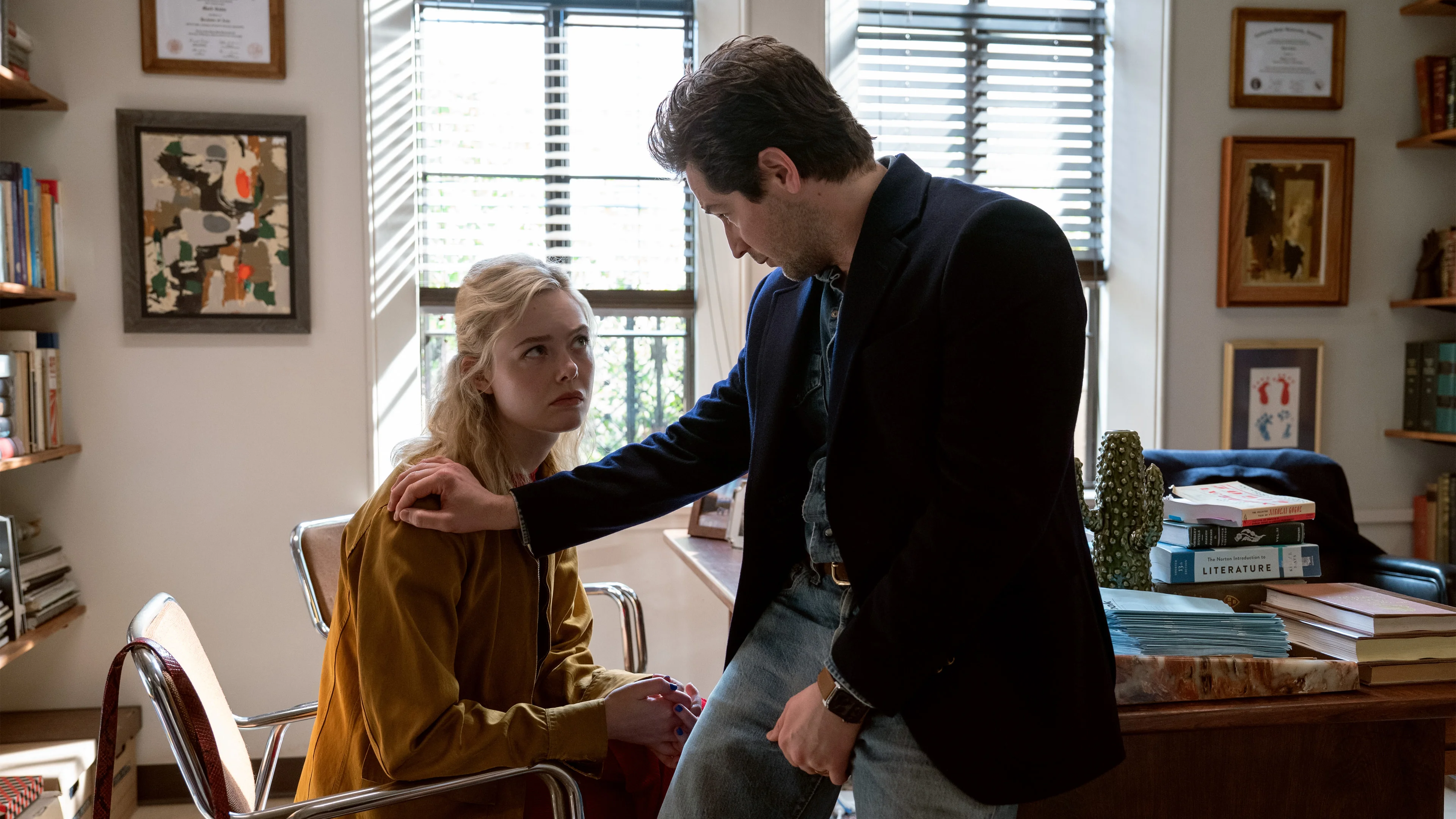 Elle Fanning as Margo sits in an office while Michael Angarano as Mark stands beside her.